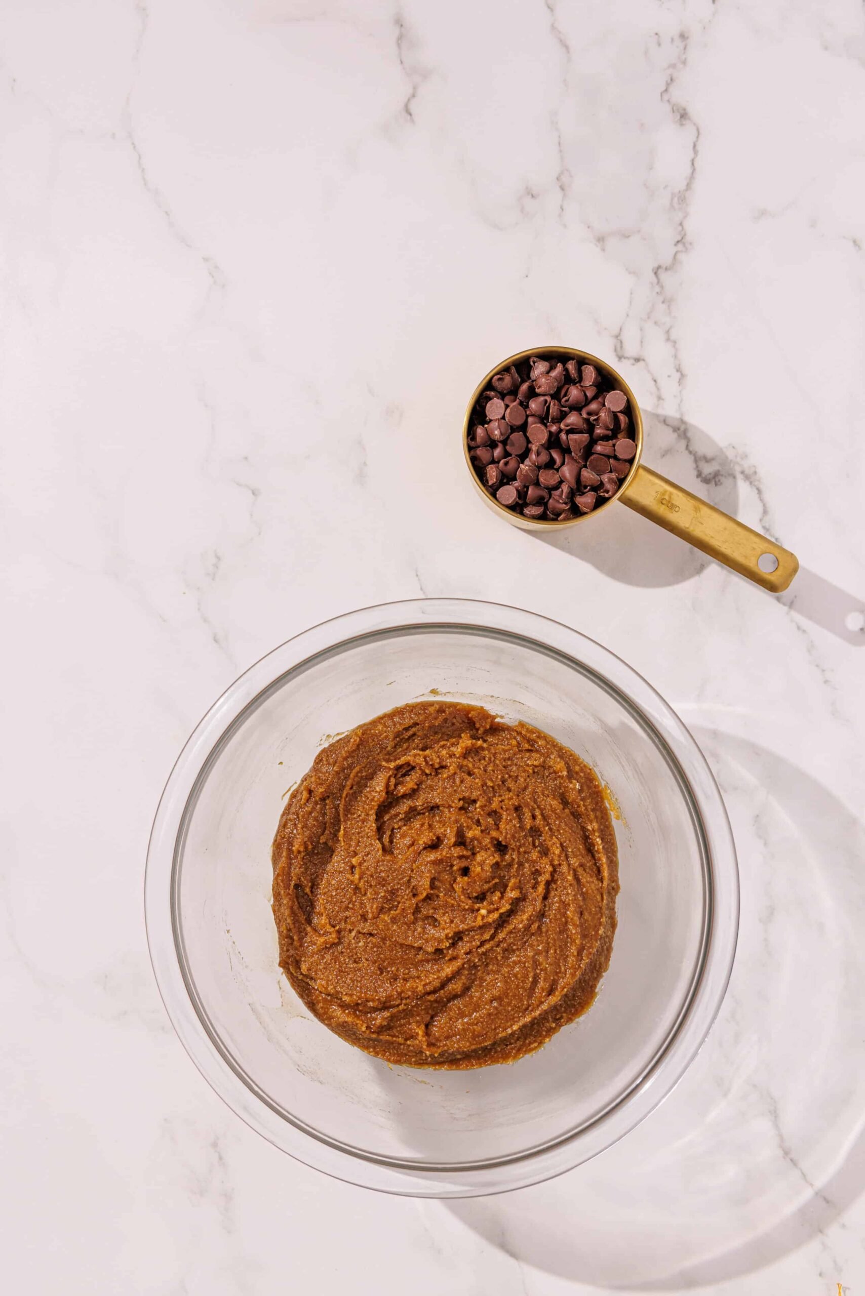 A glass bowl with vegan tahini blondie batter in it and a gold measuring cup with chocolate chips in it.