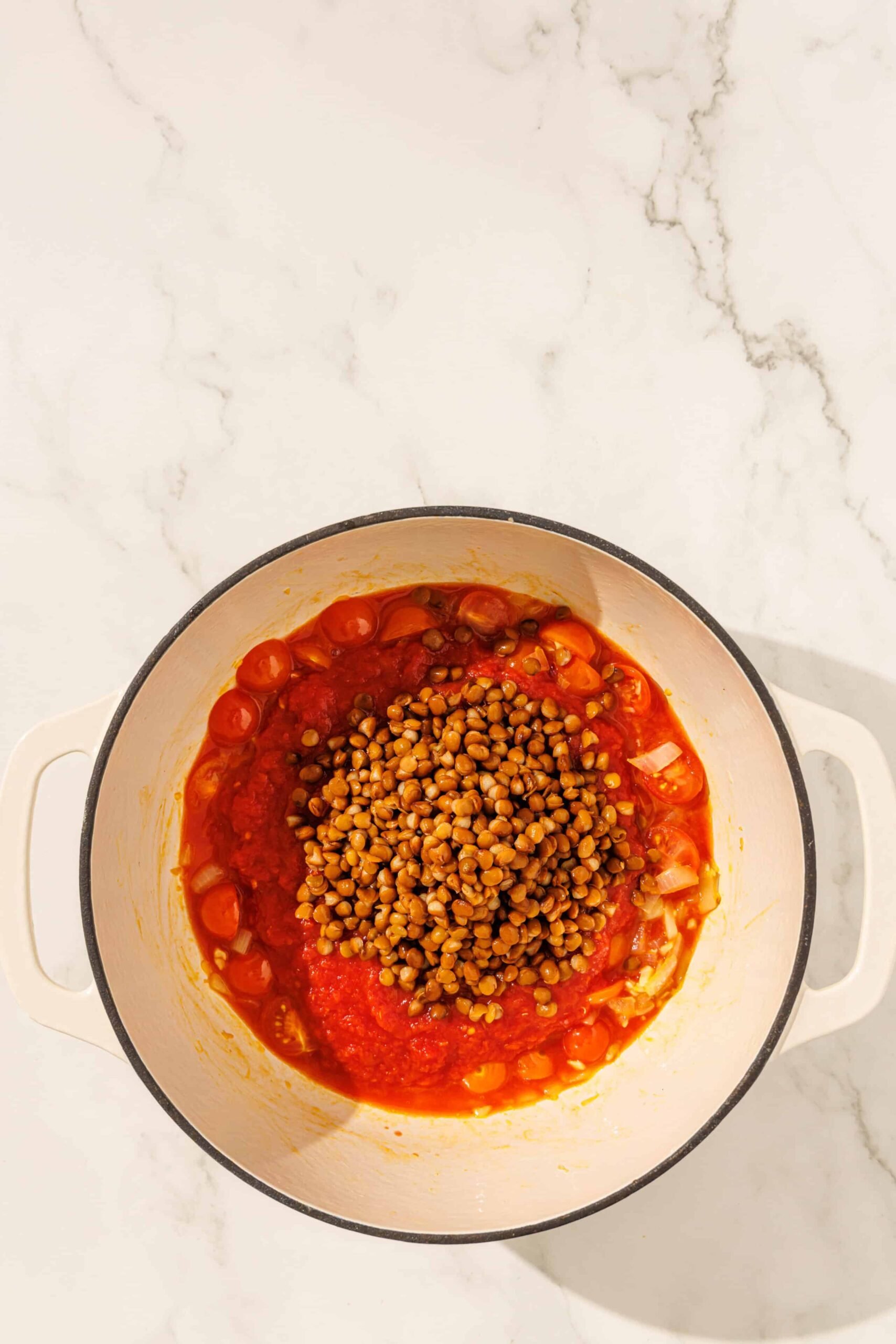 A large soup pot filled with onion, cherry tomatoes, marinara, and lentils.