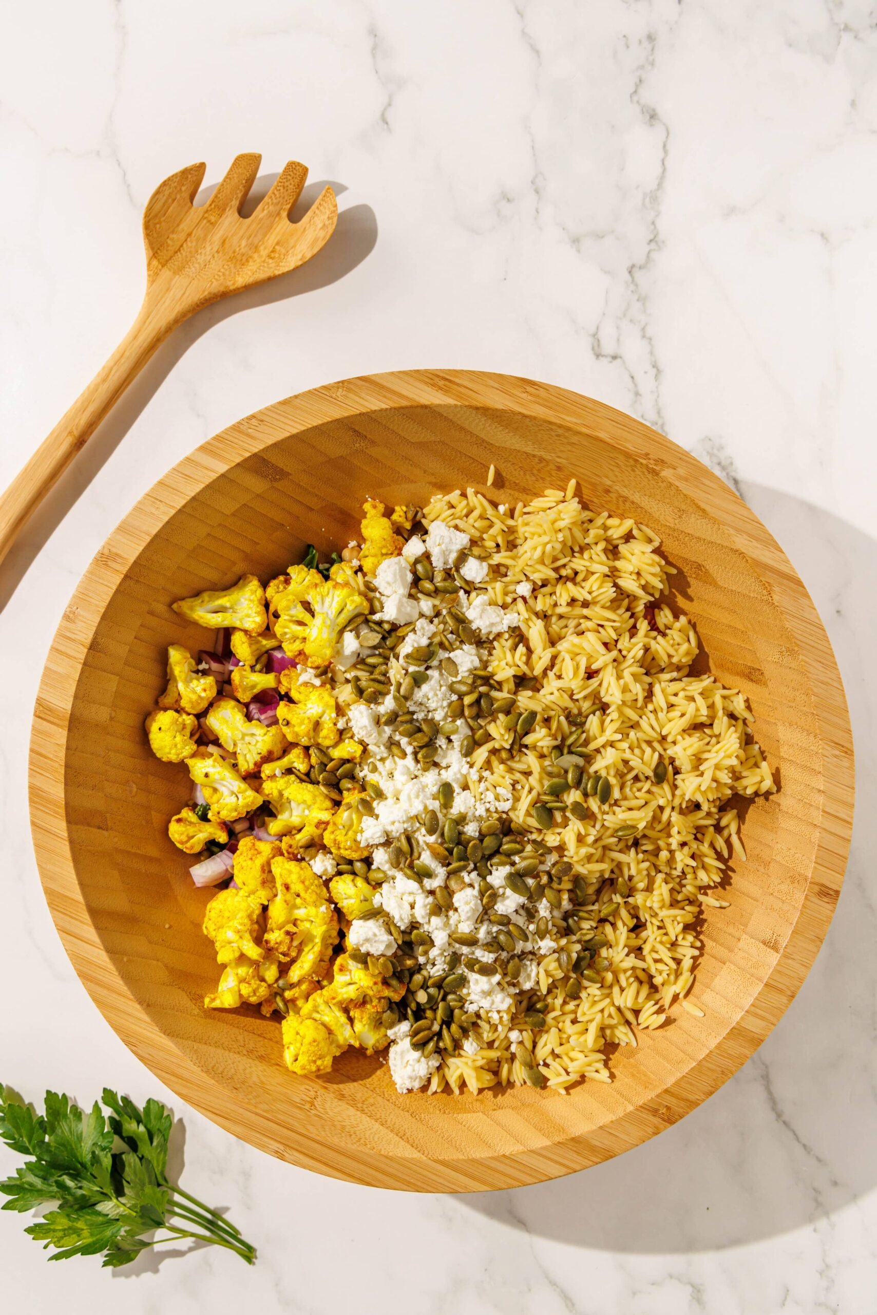A large salad bowl filled with kale, orzo, cauliflower, pumpkin seeds, feta, tomato, chickpeas, and red onion.