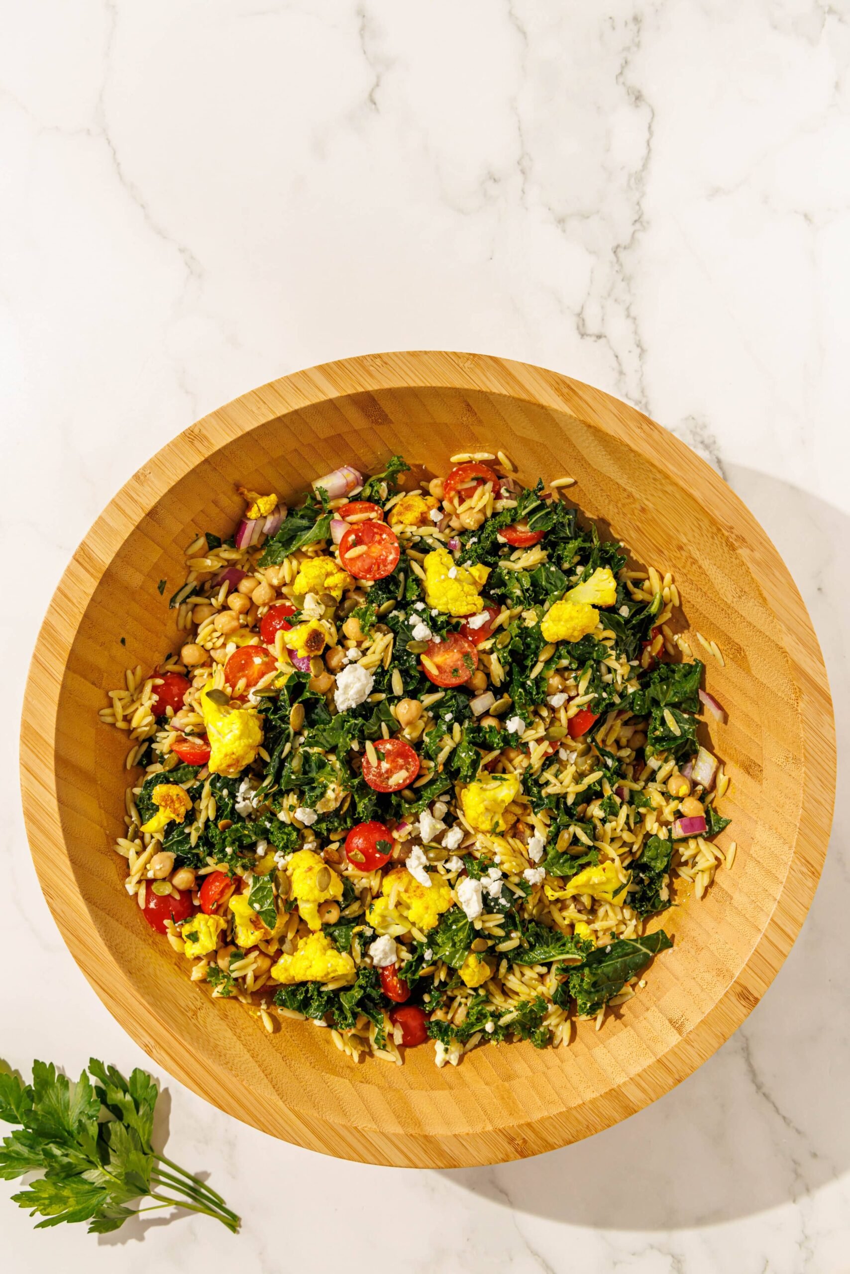 A large salad bowl filled with tossed meal prep salad and a spring of parsley beside the bowl to the left.