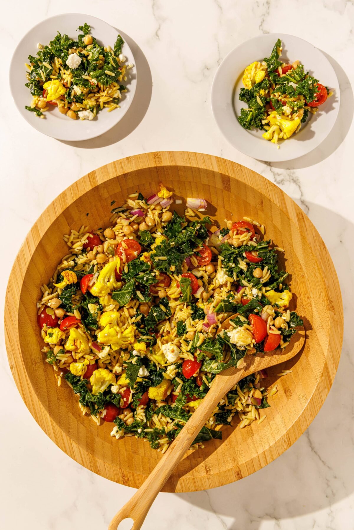 A large wooden salad bowl filled with meal prep salad and a salad spoon, and two white plates each with a single serving of meal prep salad on them.