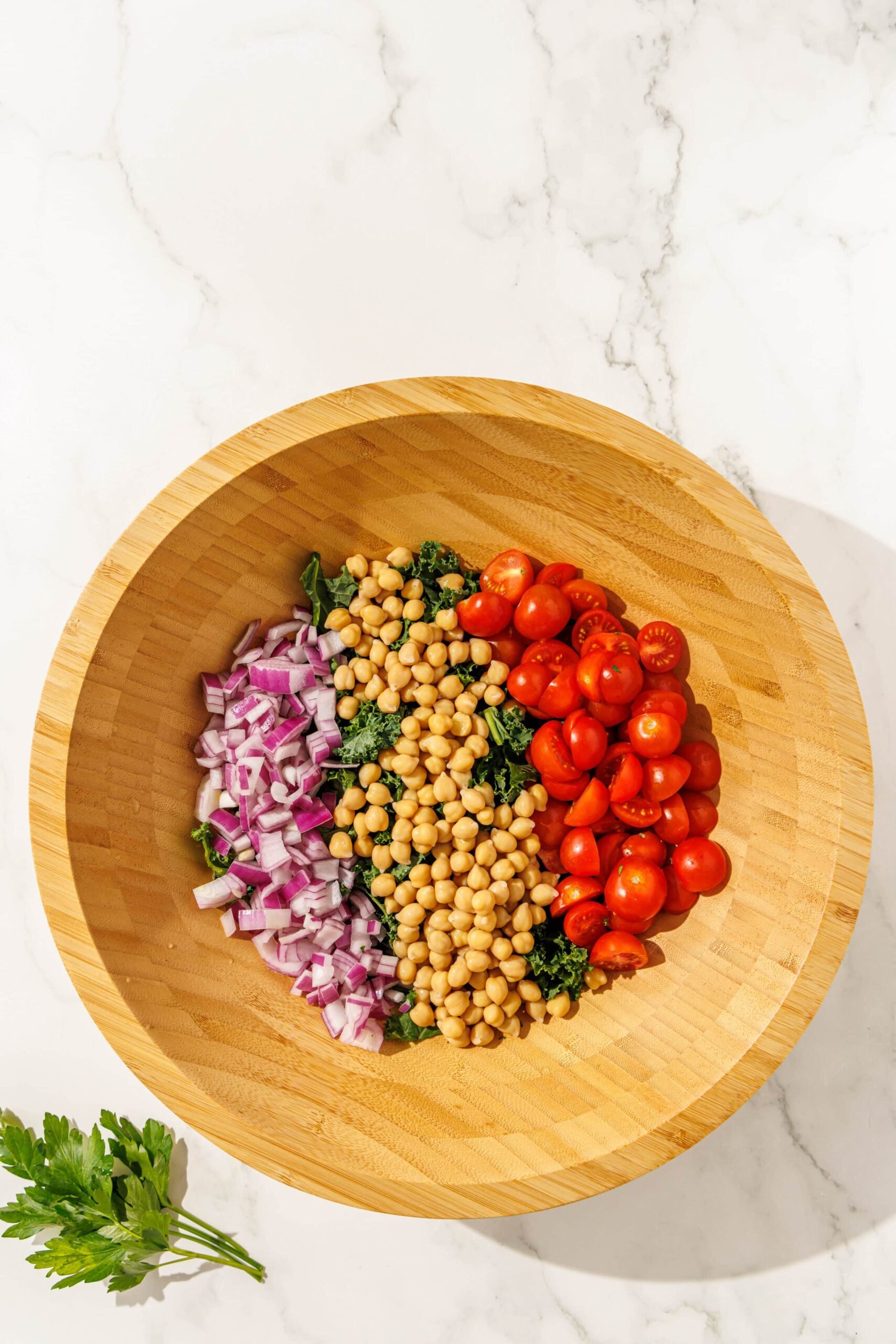 A large wooden salad bowl filled with kale, tomatoes, red onion, and chickpeas.