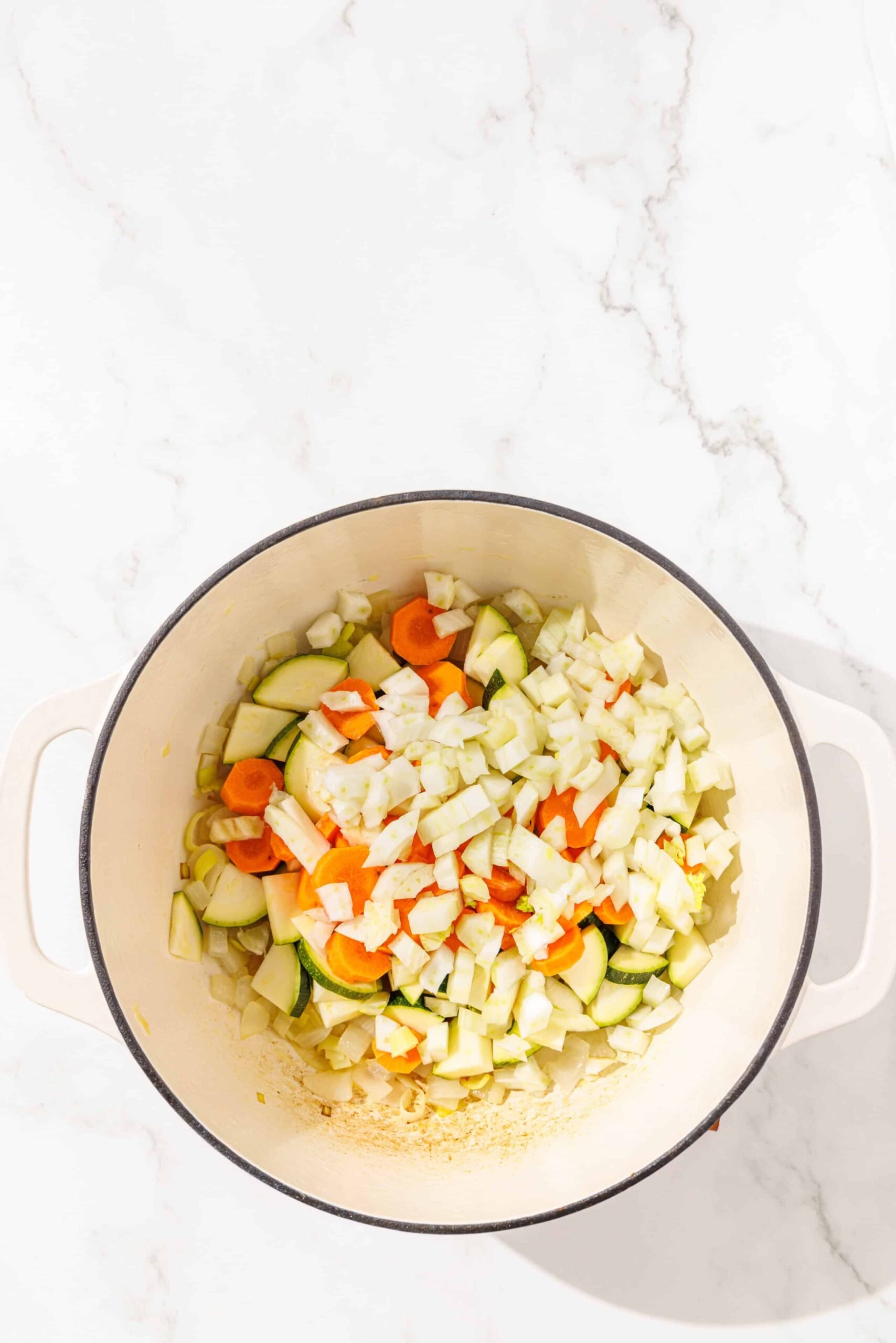 A large soup pot filled with sauteed onions, carrots, leeks, zucchini, and cauliflower.