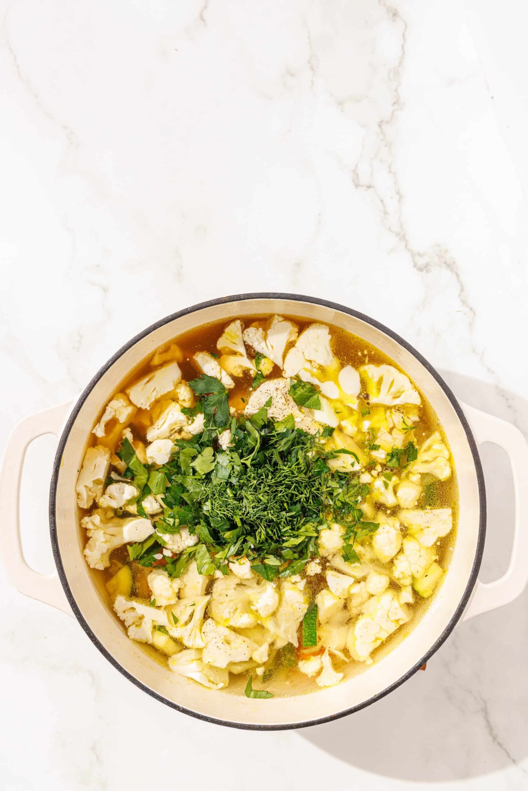 A large soup pot filled with debloat detox vegetable soup topped with fresh herbs.