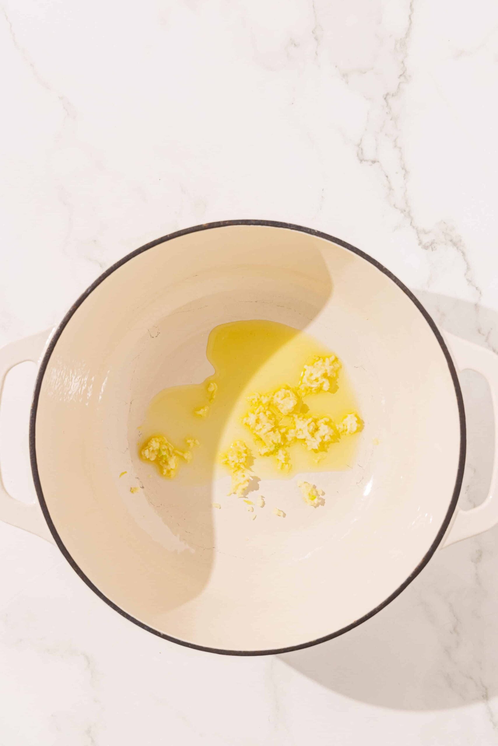 A dutch oven pot with oil in the bottom and minced garlic.