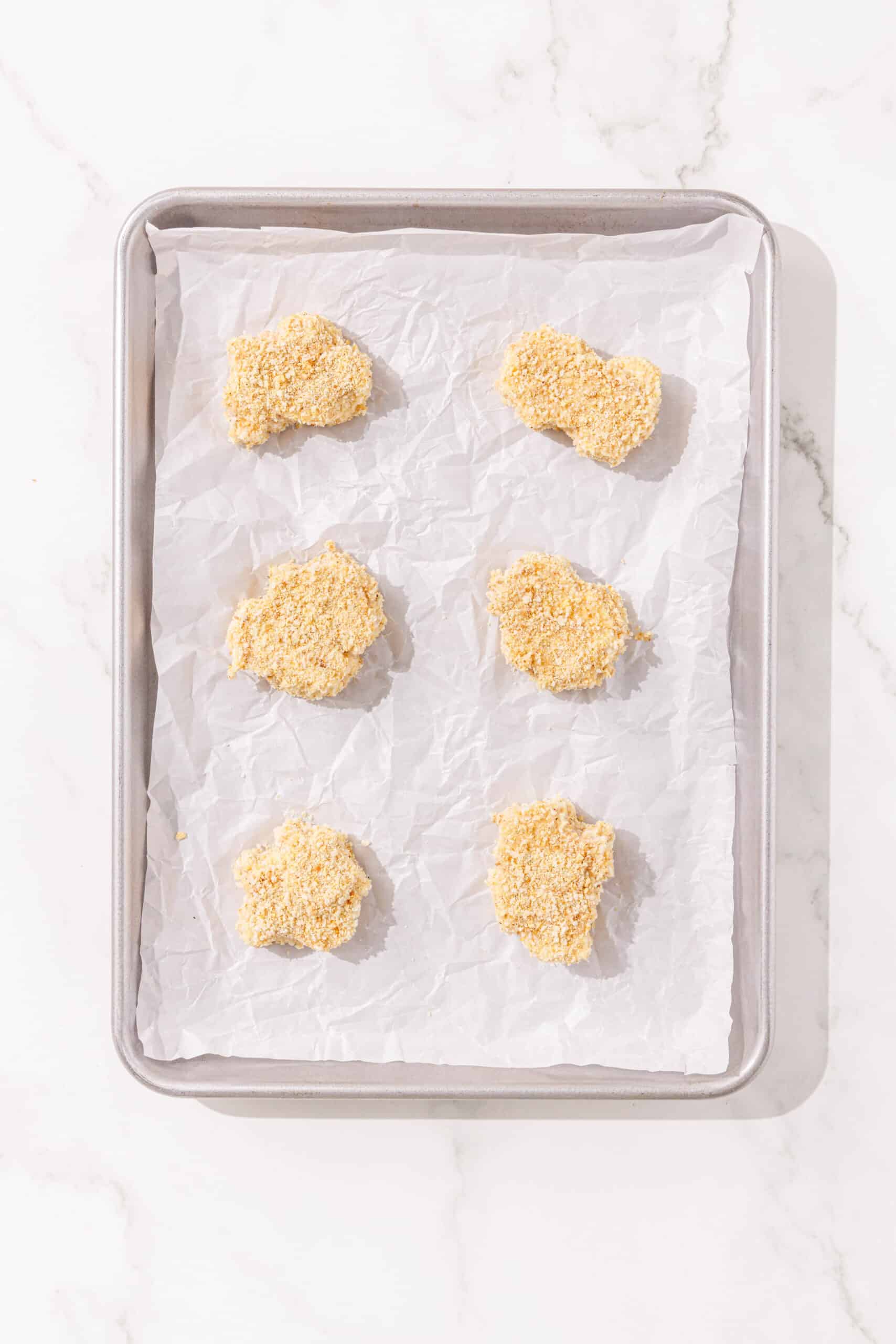 A baking sheet lined with parchment paper and 6 tofu nuggets.