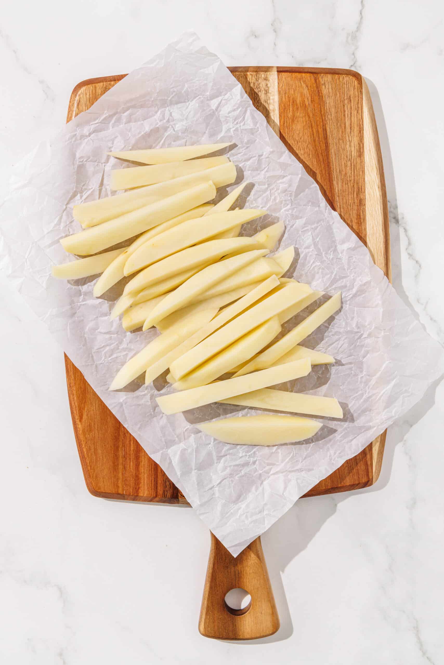 A wooden cutting board lined with parchment paper and potato fries.