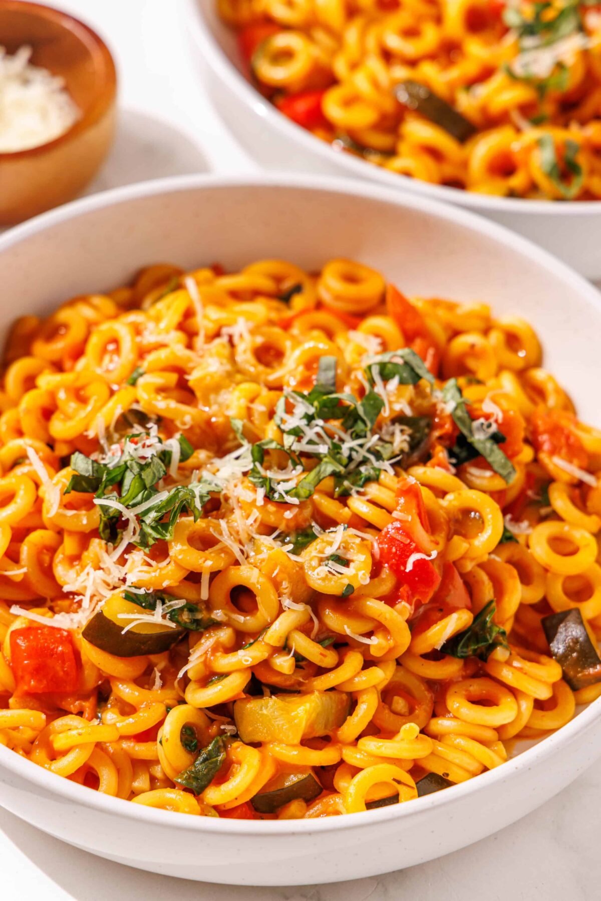 Two white bowls of one pot pasta and a small wooden bowl of parmesan.