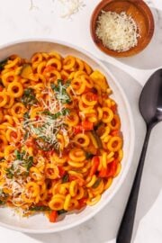 One Pot Pasta in a white bowl, a wooden bowl of parmesan, and a black spoon.