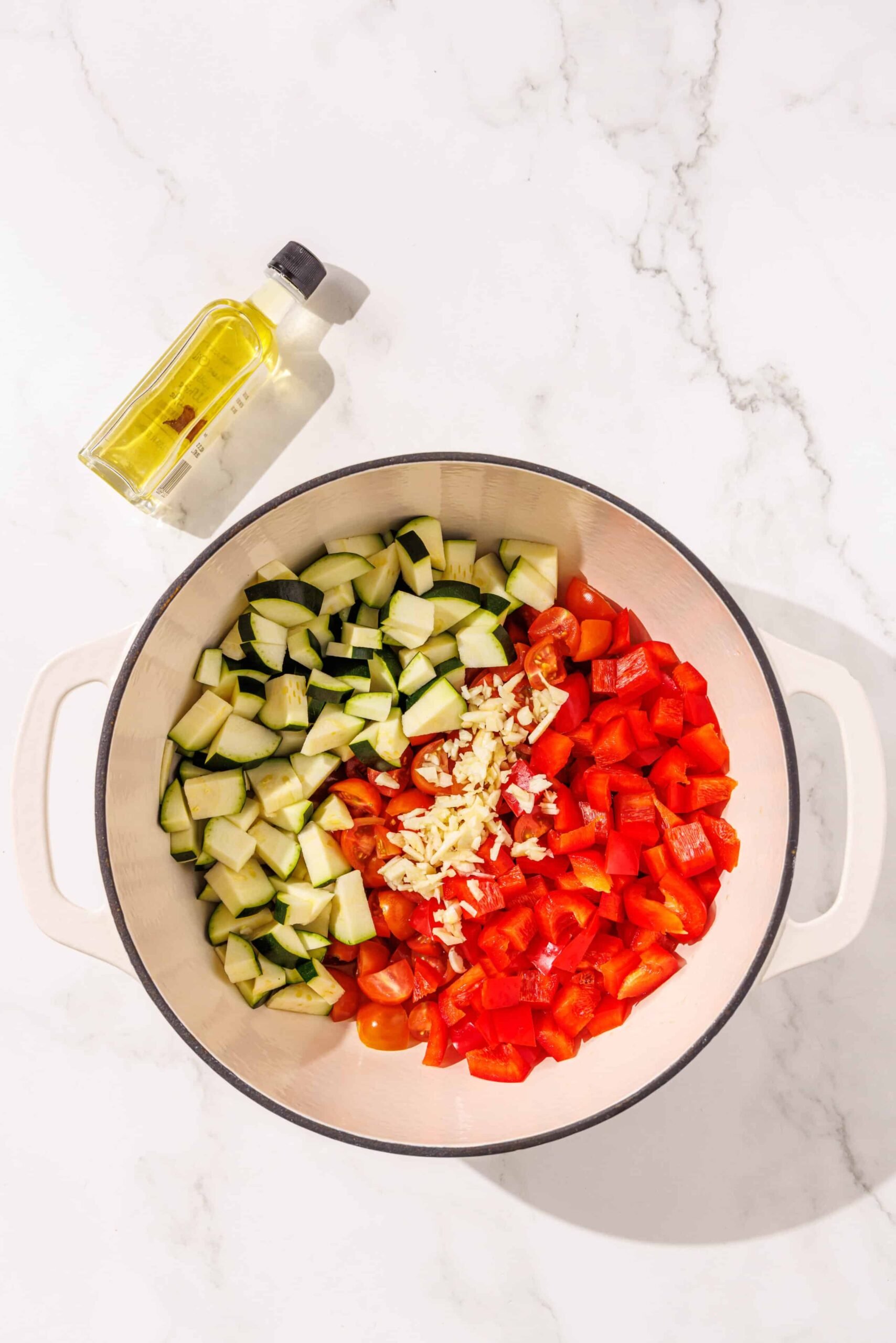 Pepper, garlic, and zuchinni in a big pot with a small bottle of oil beside the pot.
