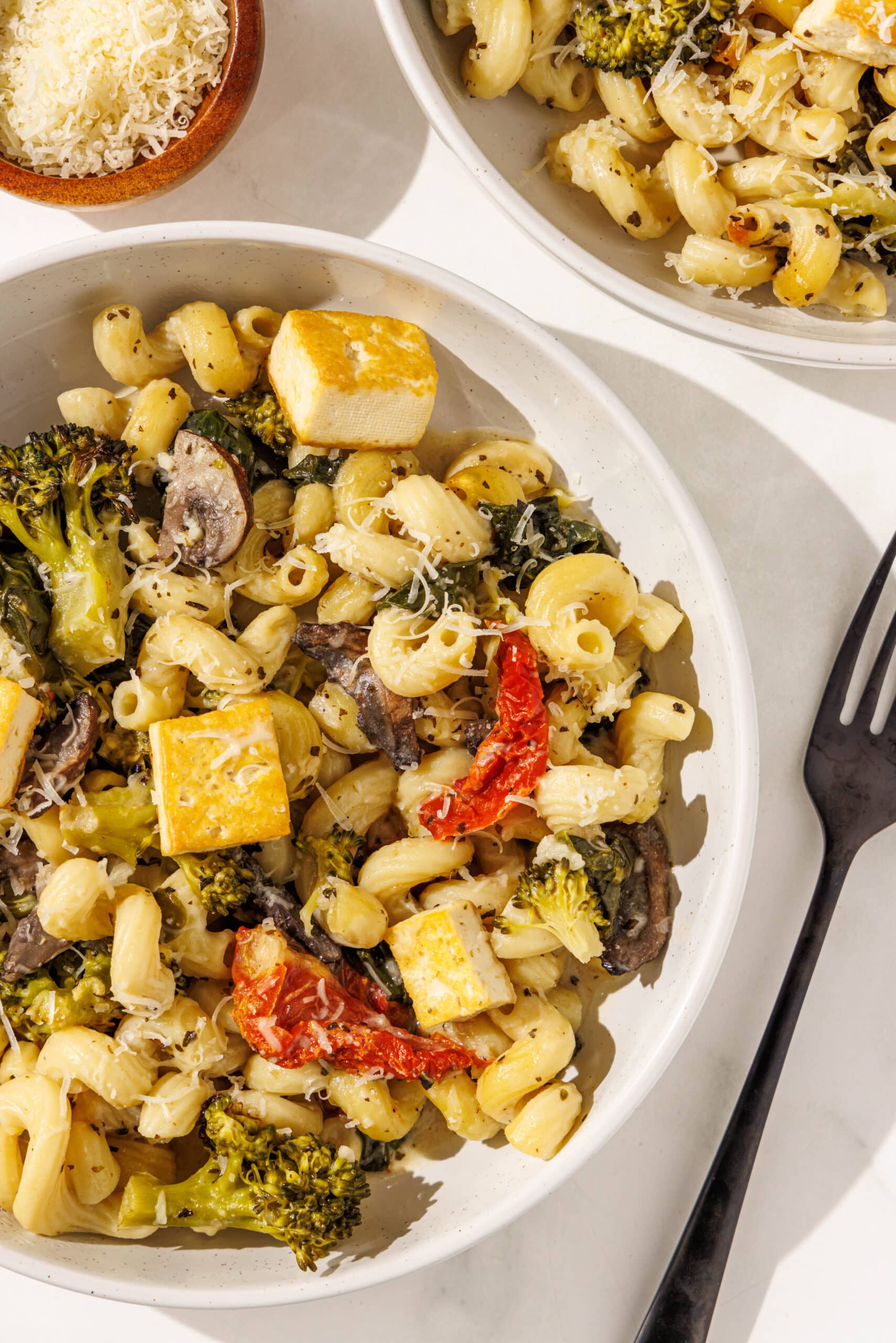 Two glass white bowls with servings of one pan tuscan pasta. A black fork is in the middle and a small wooden bowl of parmesan cheese is above.