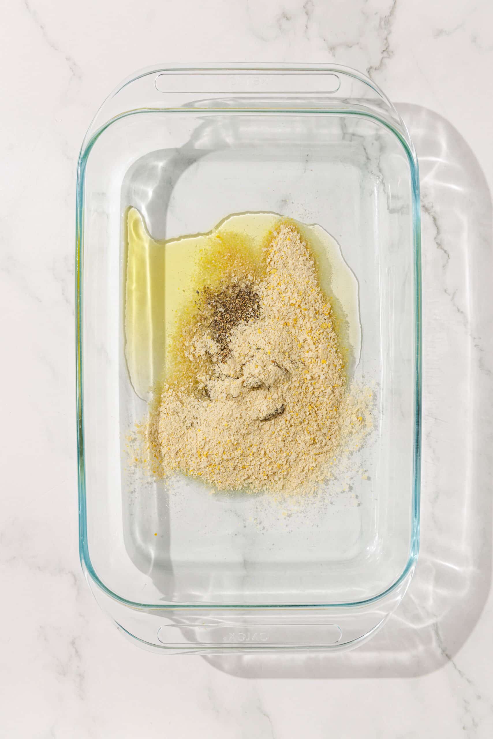 A glass 9x13 baking dish filled with spices, oil, and nutritional yeast in the center.