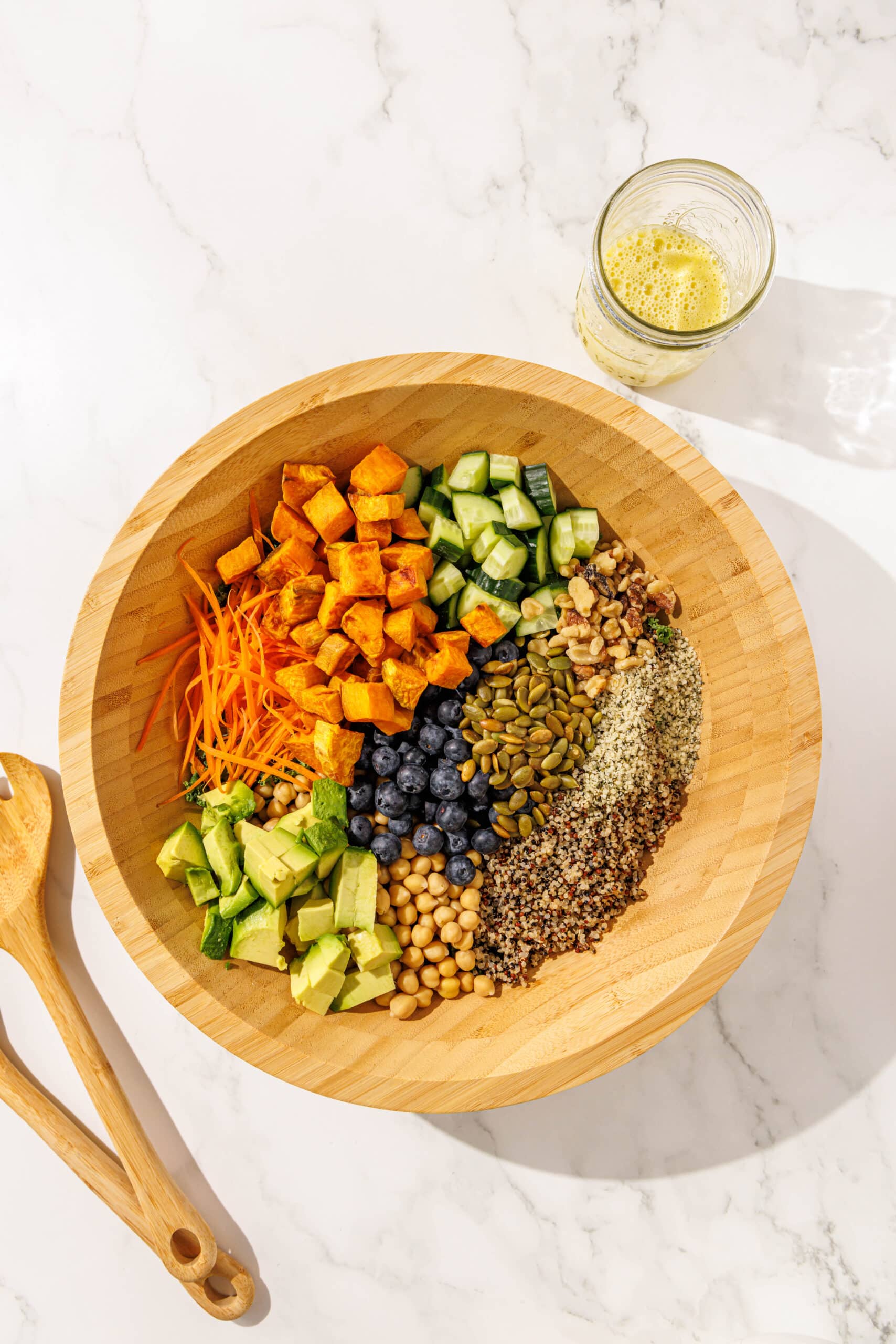 A wooden salad bowl filled with longevity salad. To the left of the bowl is two wooden spoons and to the right is a glass jar filled with salad dressing.