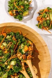 A wood bowl filled with Longevity Salad with two smaller white plates beside it with a serving of salad on each. There is a set of wooden spoons in the large salad bowl.