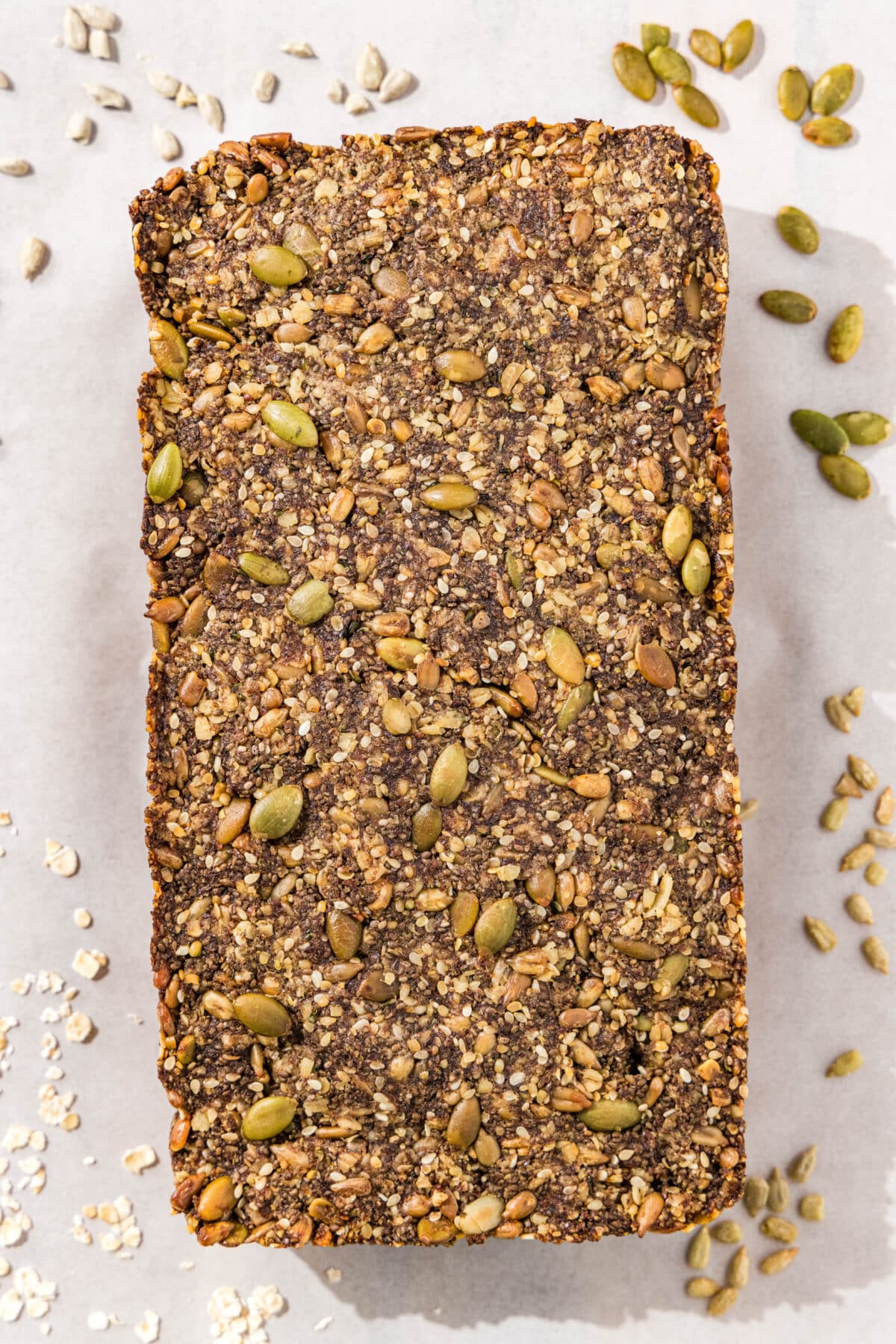 Close up of the seedy bread loaf on a piece of parchment paper with pumpkin and sunflower seeds scattered around it.