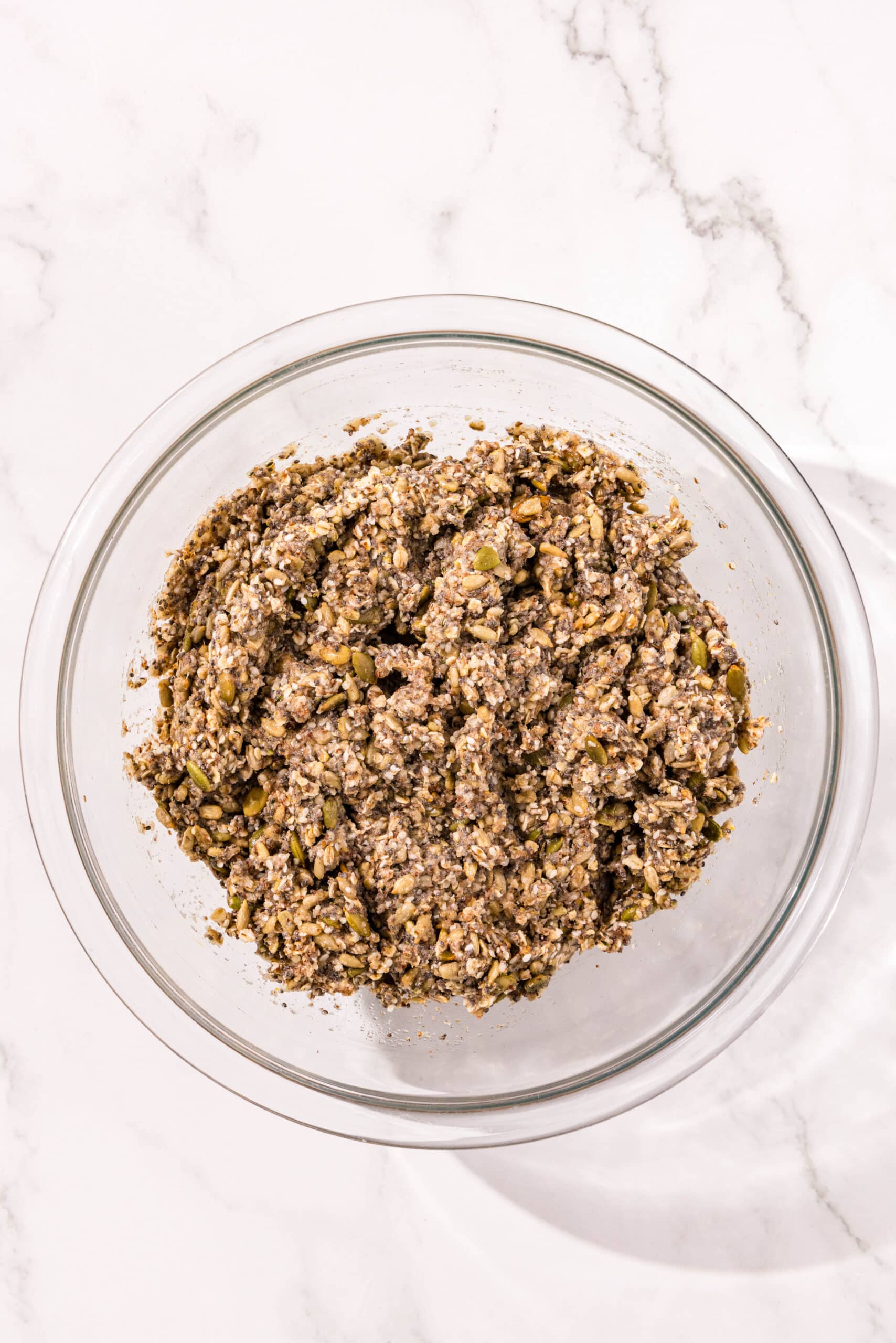 Seedy bread dough mixed in a large glass bowl and ready to be baked.