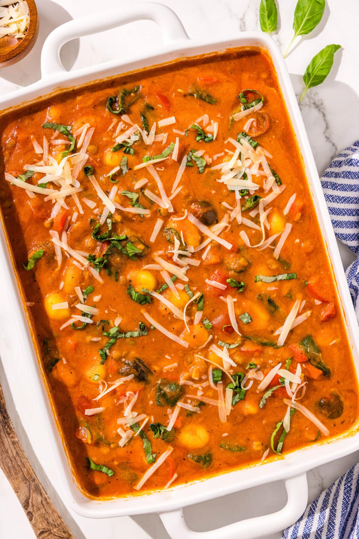 A white rectangular casserole dish filled with the one pan gnocchi. The gnocchis are cooked and covered in marinara and topped with vegan parmesan and basil.