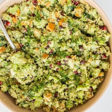 Quinoa broccoli salad in a large wooden bowl with a silver spoon in it.