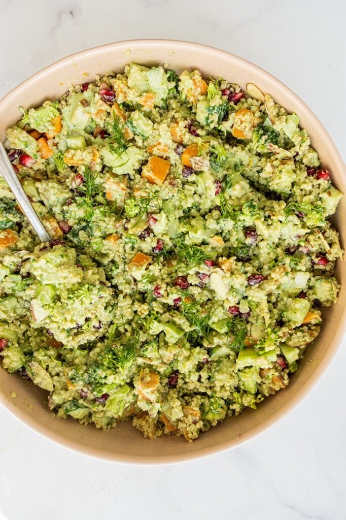 Quinoa broccoli salad in a large wooden bowl with a silver spoon in it.