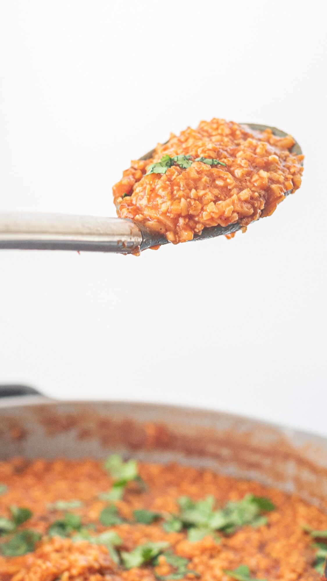 One Pan Creamy Mexican Cauliflower Rice on a silver spoon over the large pan filled with remaining cauliflower rice, garnished with cilantro.