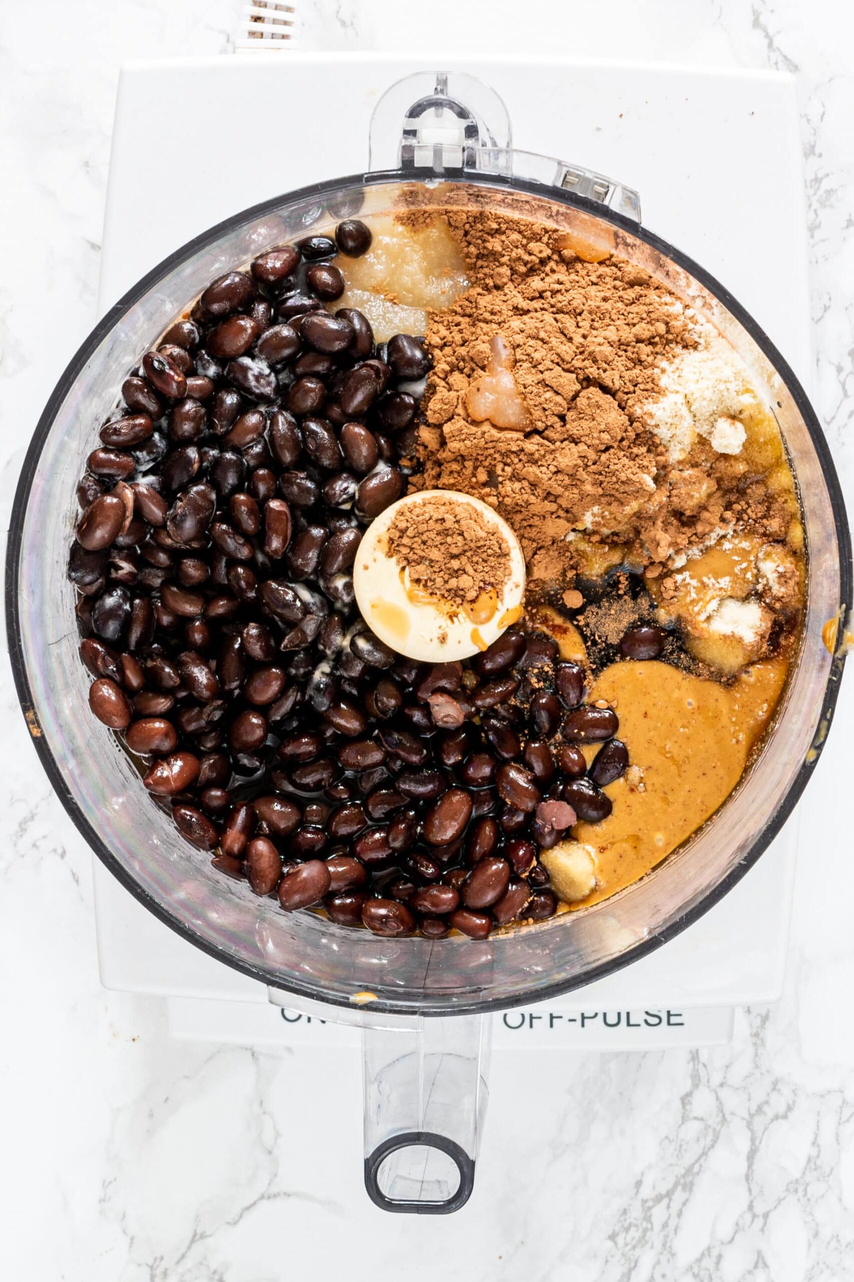 A food processor filled with black beans, peanut butter, cacao powder, and almond flour.