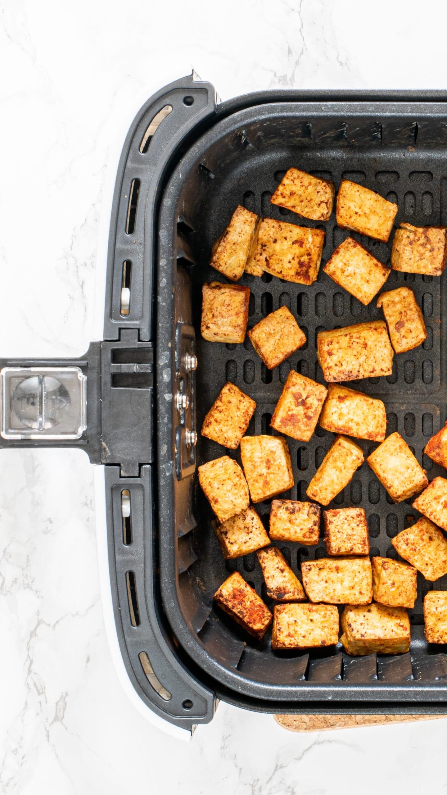 A black air fryer basket filled with tofu nuggets ready to be cooked.