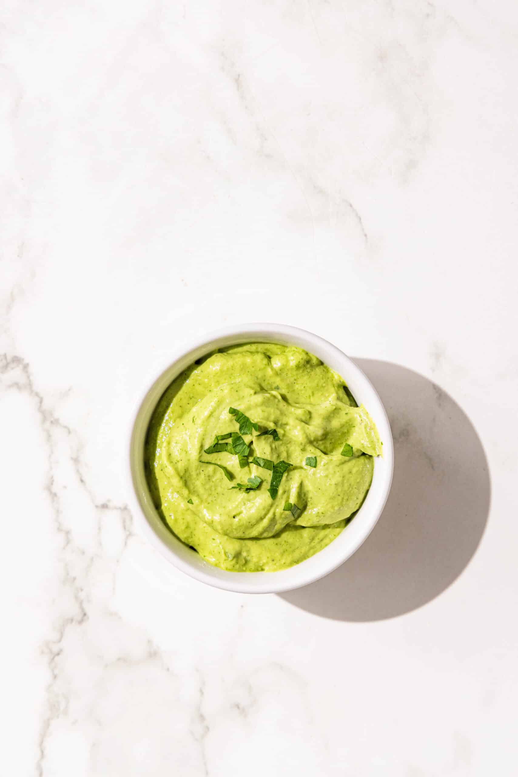 A small bowl of green goddess avocado sauce garnished with cilantro.