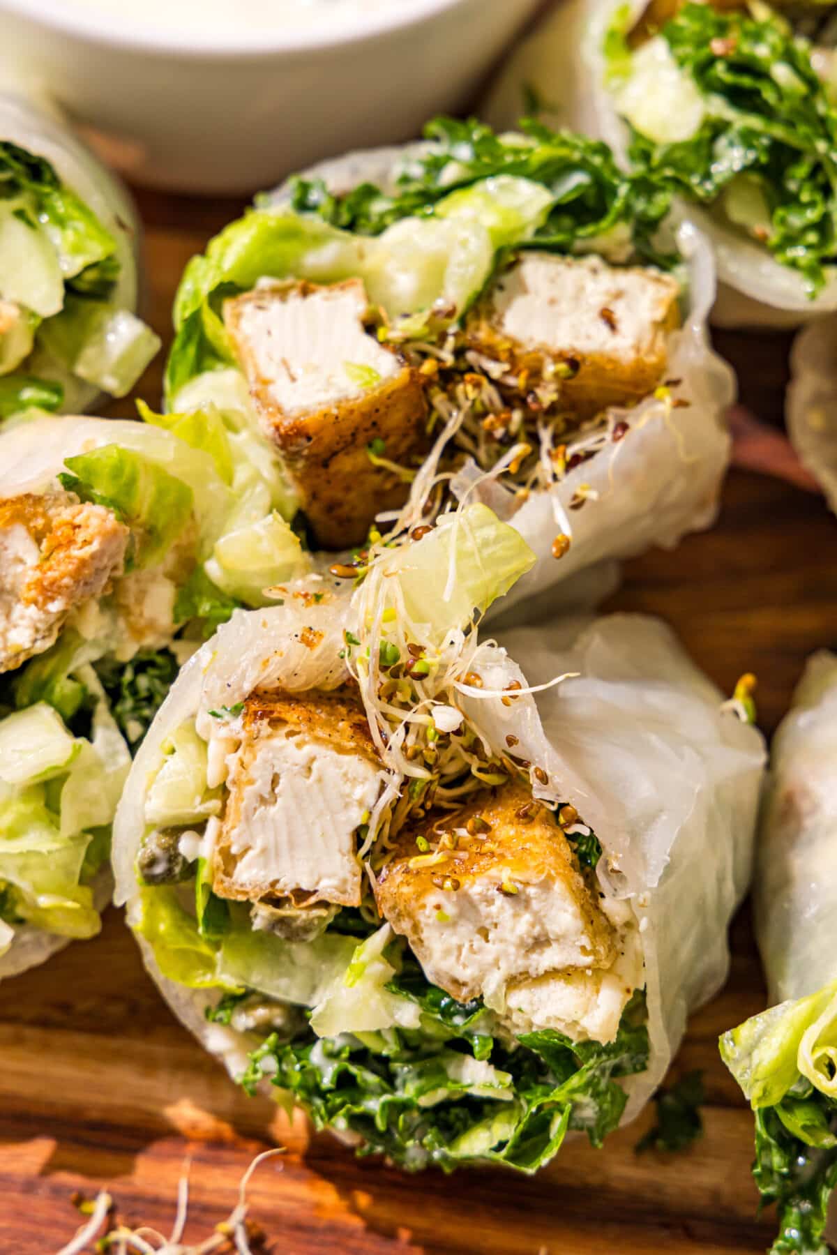 A spring roll filled with kale caesar salad, sprouts, and crispy tofu cut in half.