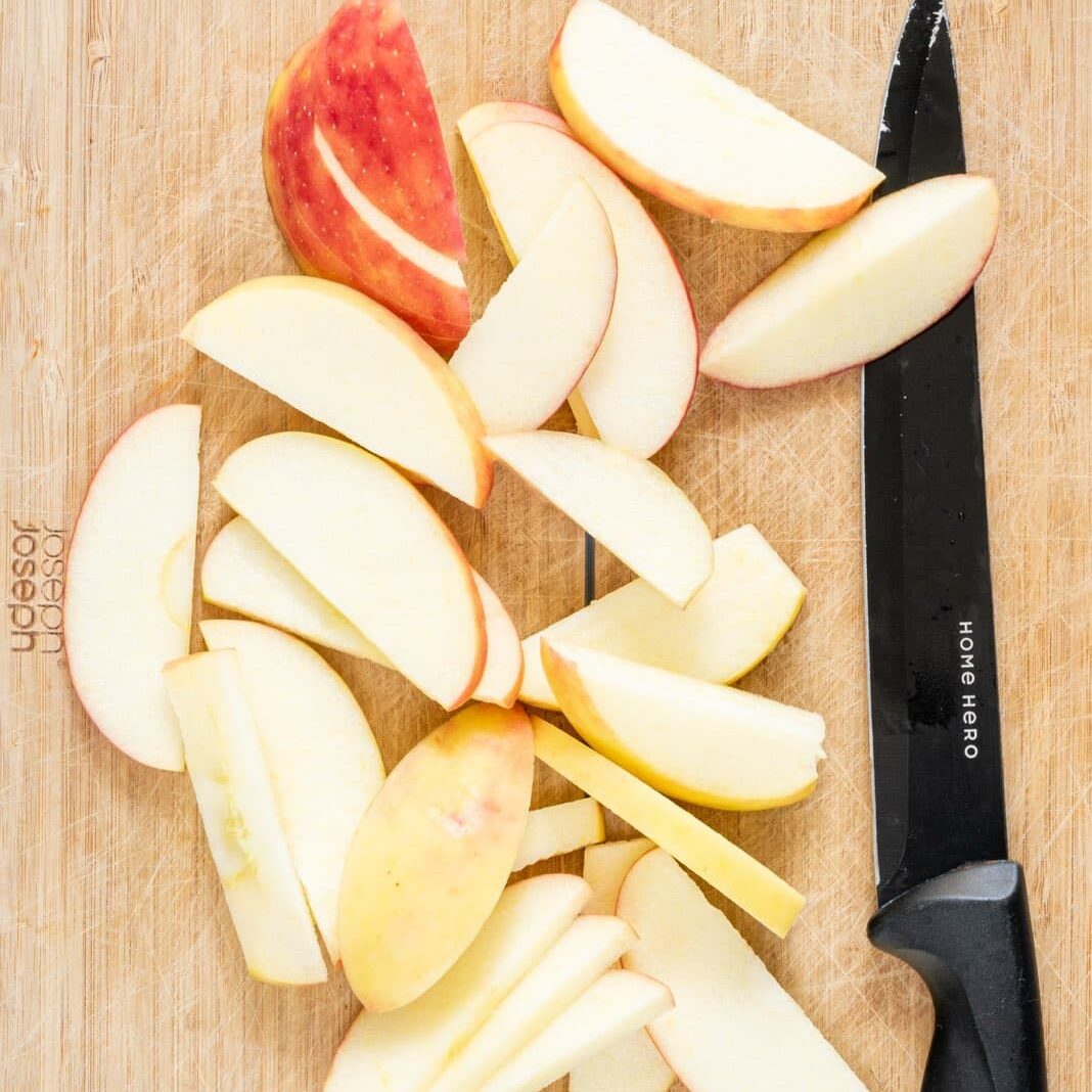 A wooden cutting board with a knife on it and sliced apples.