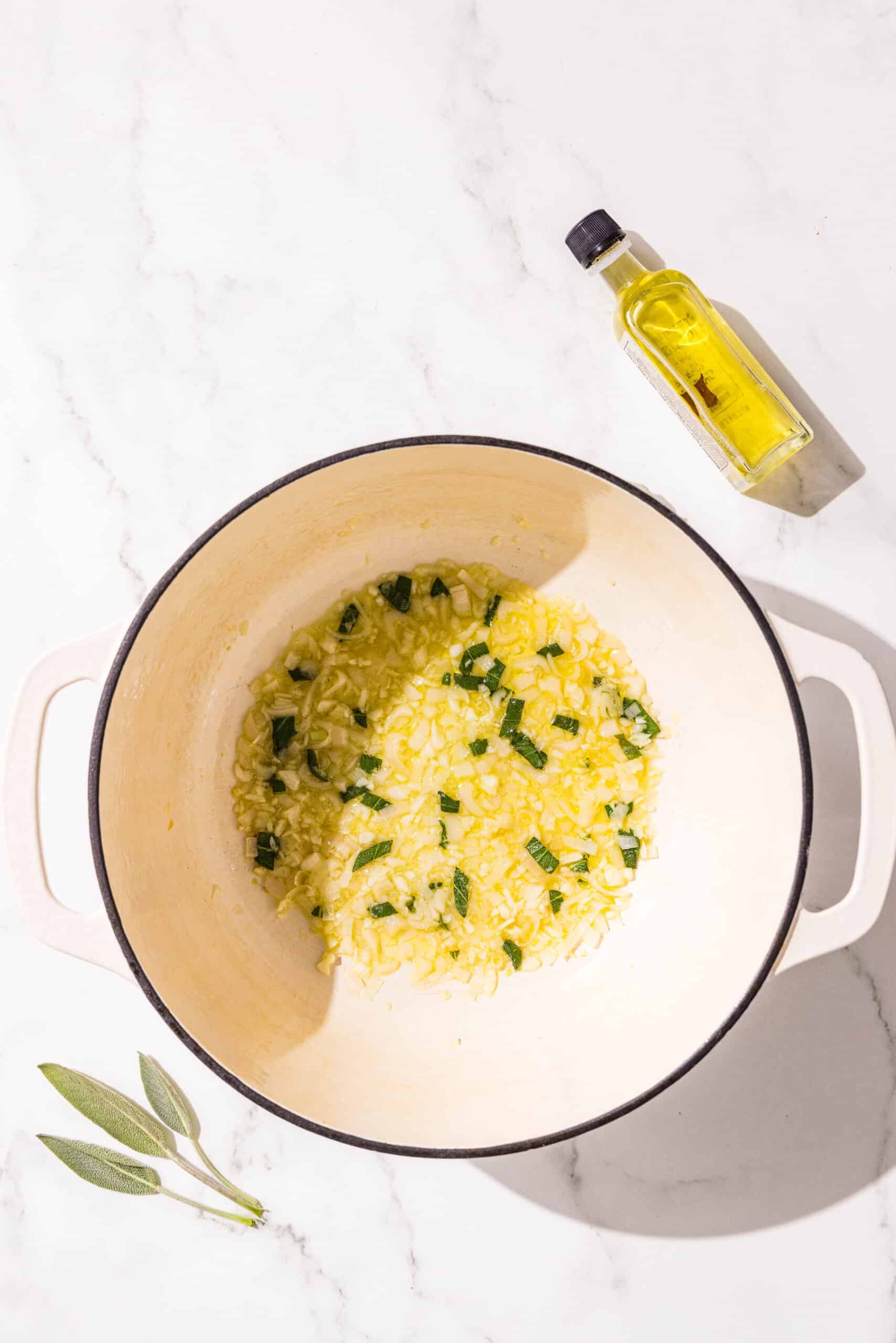 A large pot filled with oil, fresh sage, and minced garlic. Beside the pot is a small jar of oil and a fresh piece of sage.