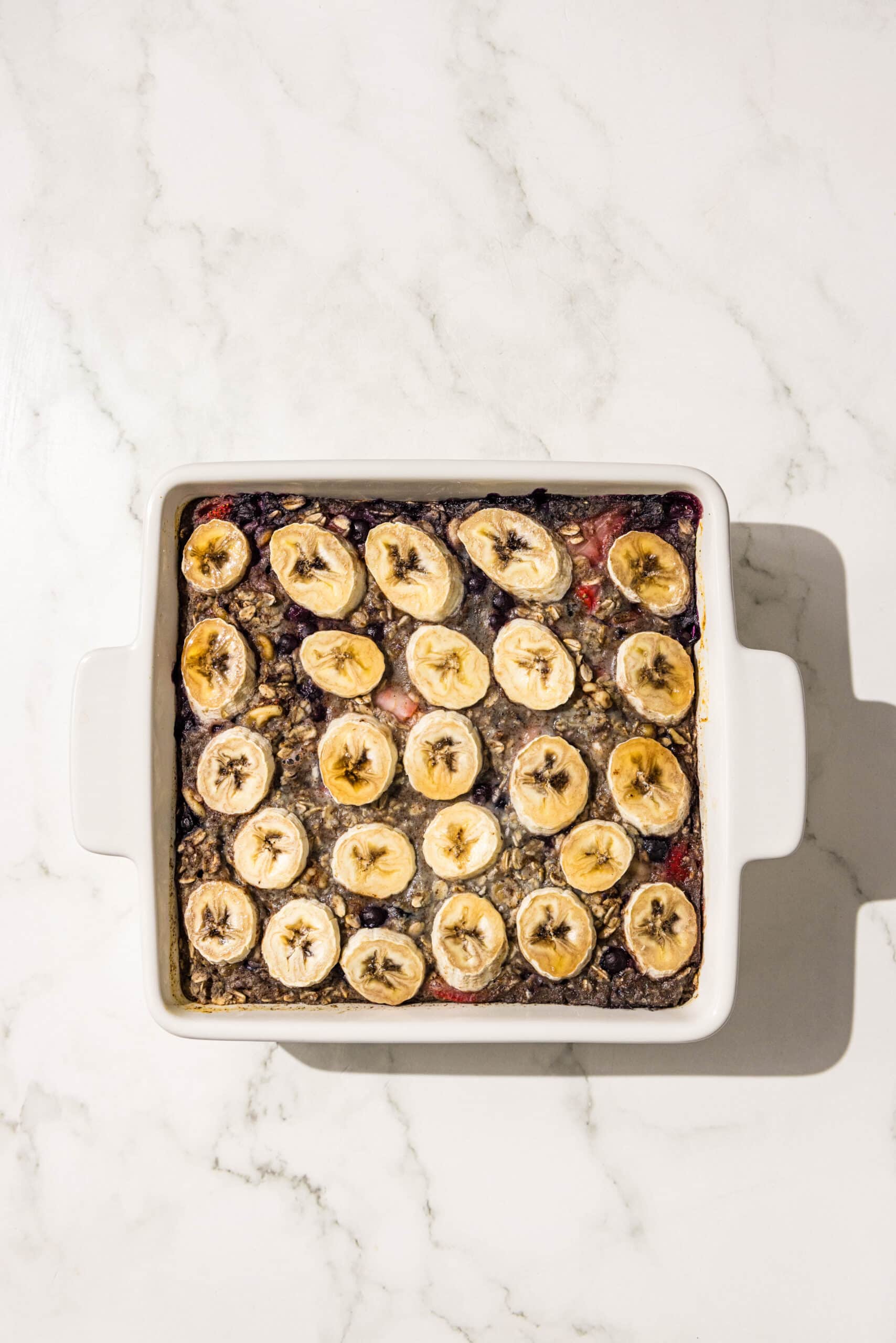A 9x9 baking dish of blueberry baked oatmeal topped with banana slices.