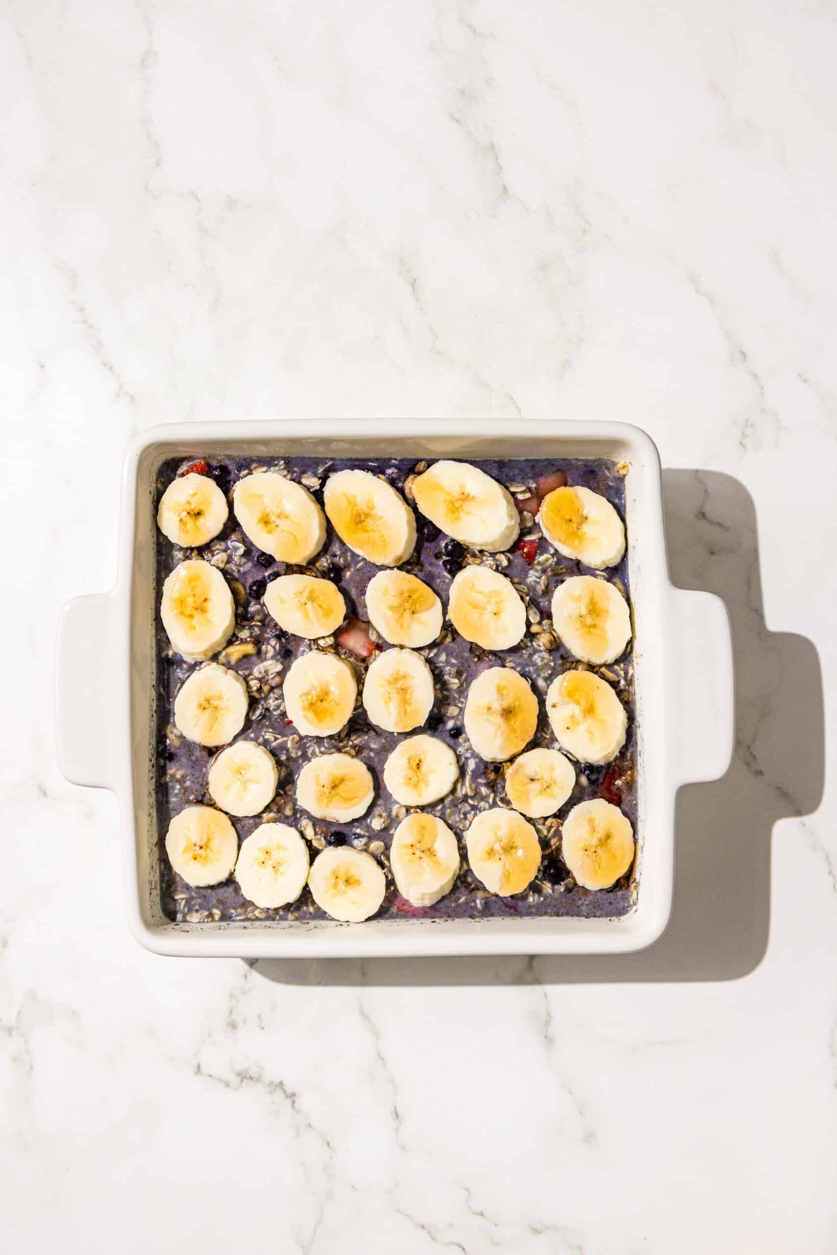 A 9x9 baking dish of blueberry baked oatmeal topped with banana slices.
