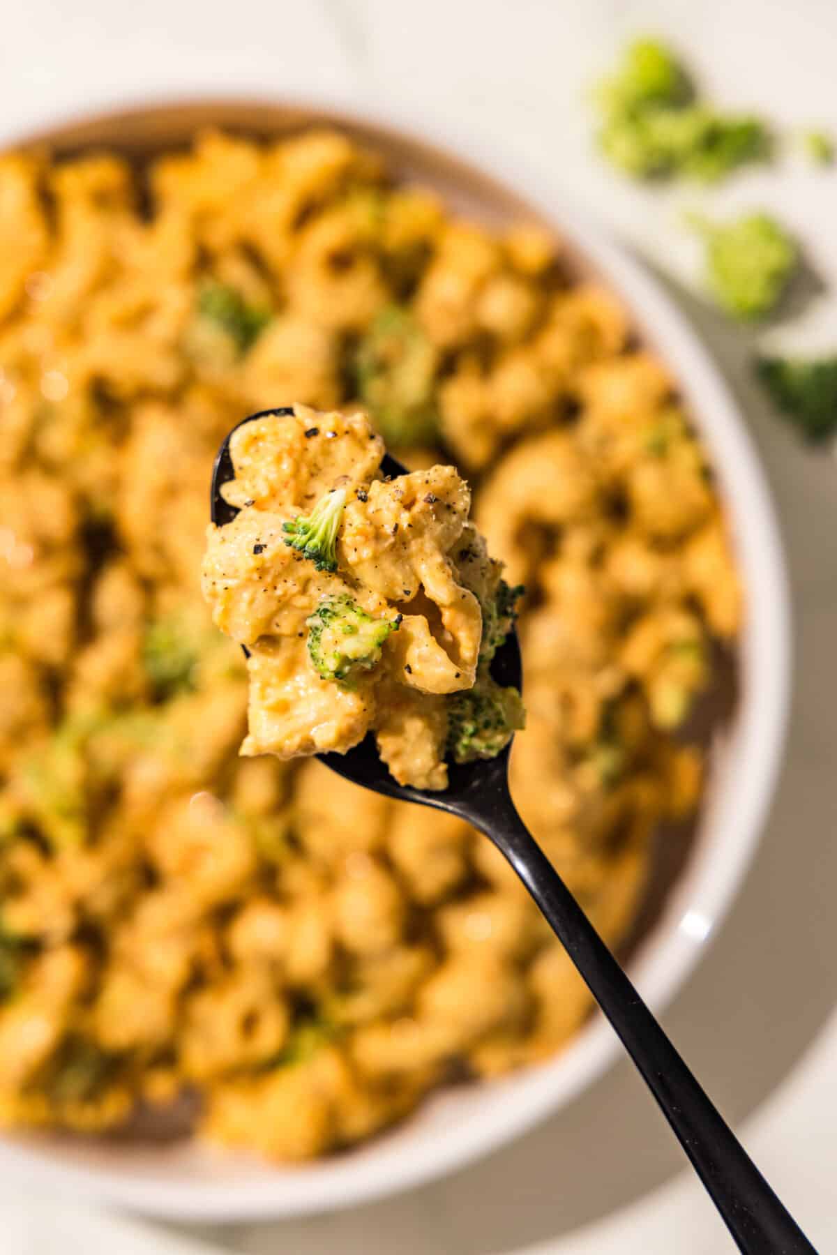 A bowl of mac and cheese with broccoli and a black spoon filled with a bite of mac and cheese.