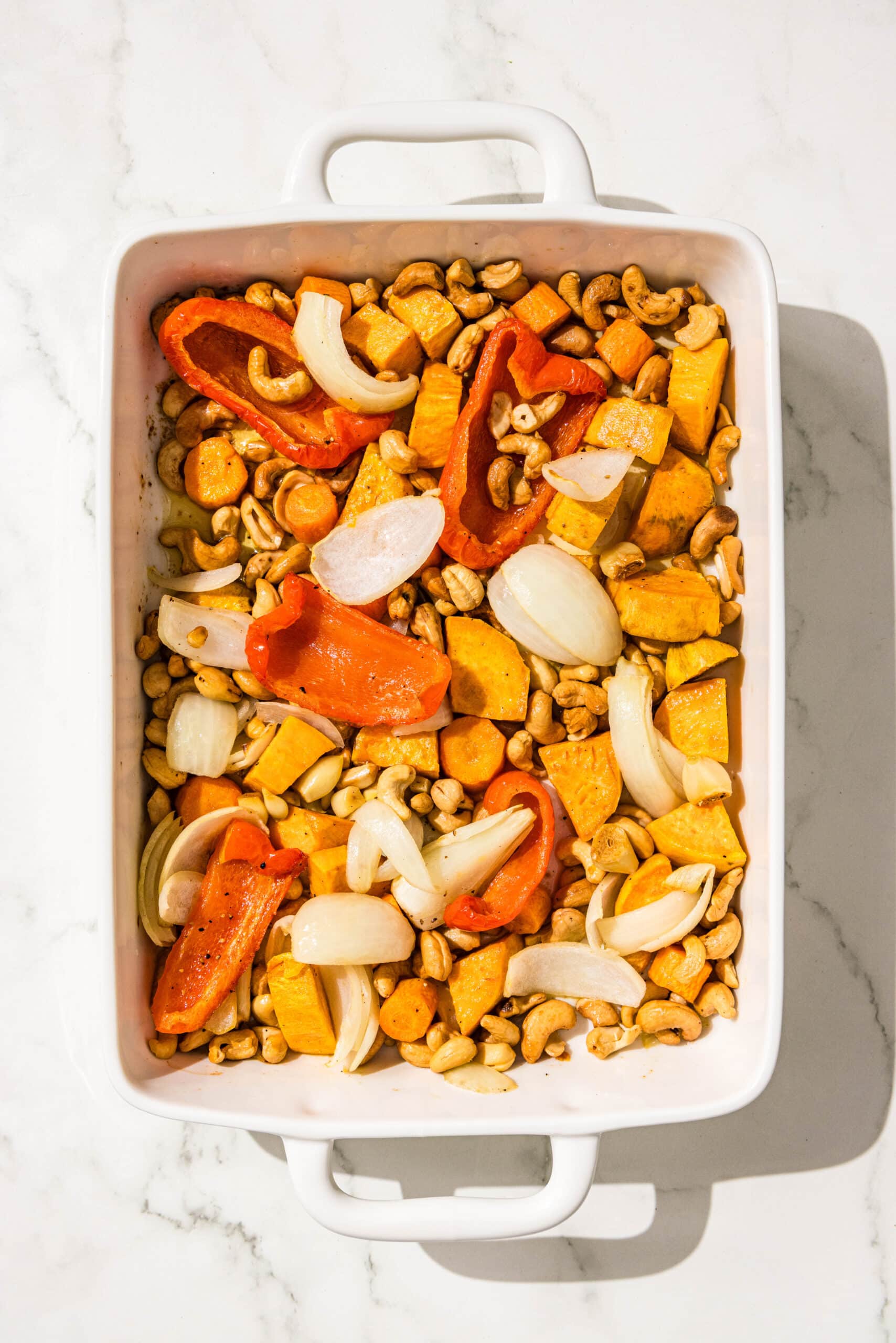 Roasted bell pepper, sweet potato, onion, and cashews in a 9x13 casserole dish.