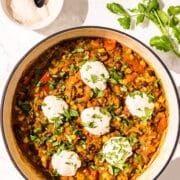 A large pot of a rice and bean mixture topped with cilantro and sour cream. Beside the pot is a small bowl of sour cream and a sprig of fresh cilantro.