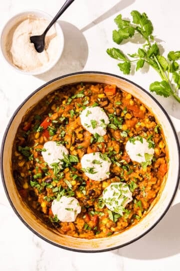 A large pot of a rice and bean mixture topped with cilantro and sour cream. Beside the pot is a small bowl of sour cream and a sprig of fresh cilantro.