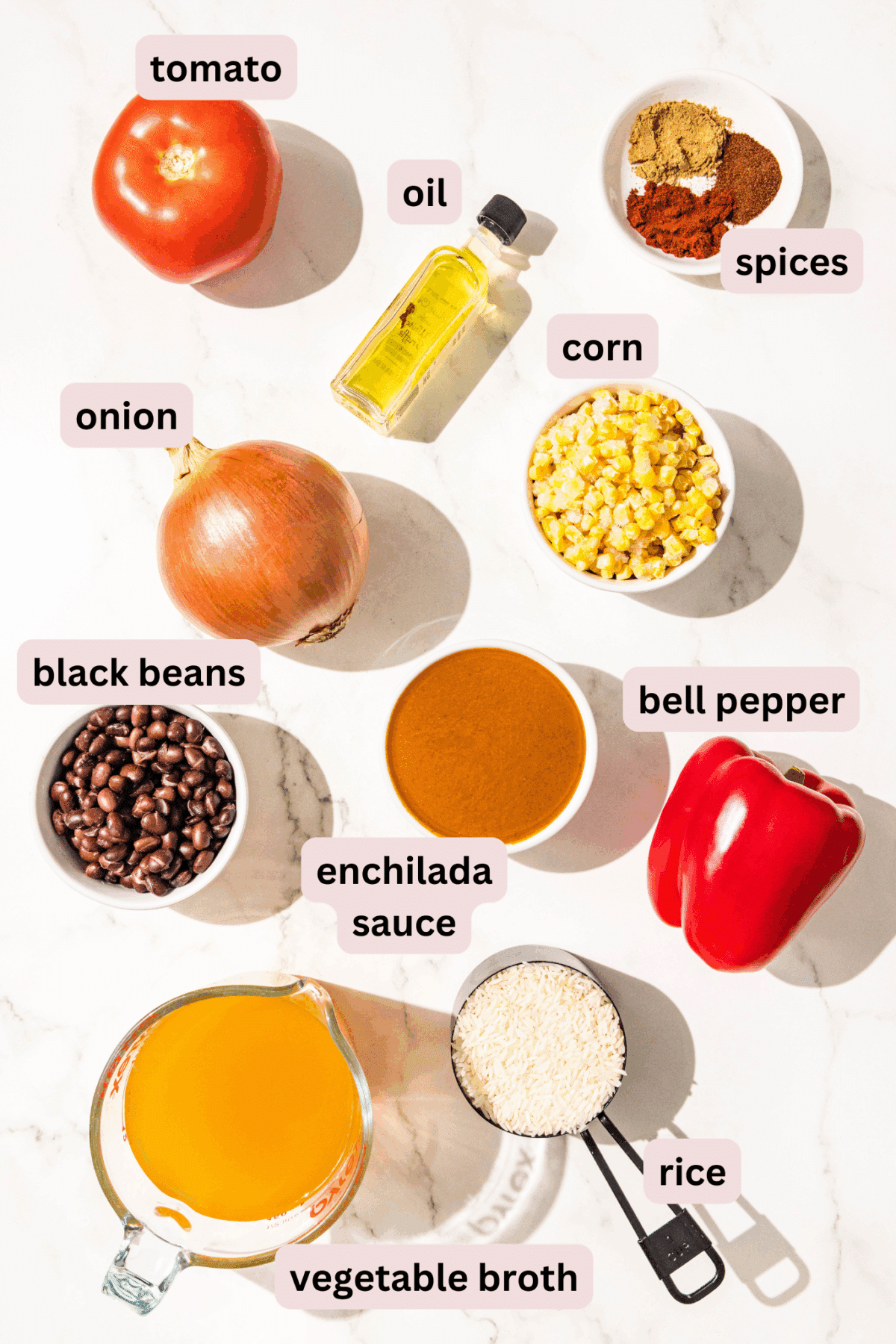 Ingredients laid out on the counter in bowls and labeled including: tomato, oil, spices, corn, onion, bell pepper, enchilada sauce, black beans, rice, and vegetable broth.
