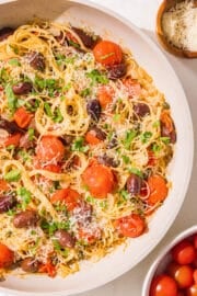 A bowl of spaghetti with tomatoes, kalamata olives, topped with fresh parsley and parmesan.