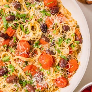 A bowl of spaghetti with tomatoes, kalamata olives, topped with fresh parsley and parmesan.
