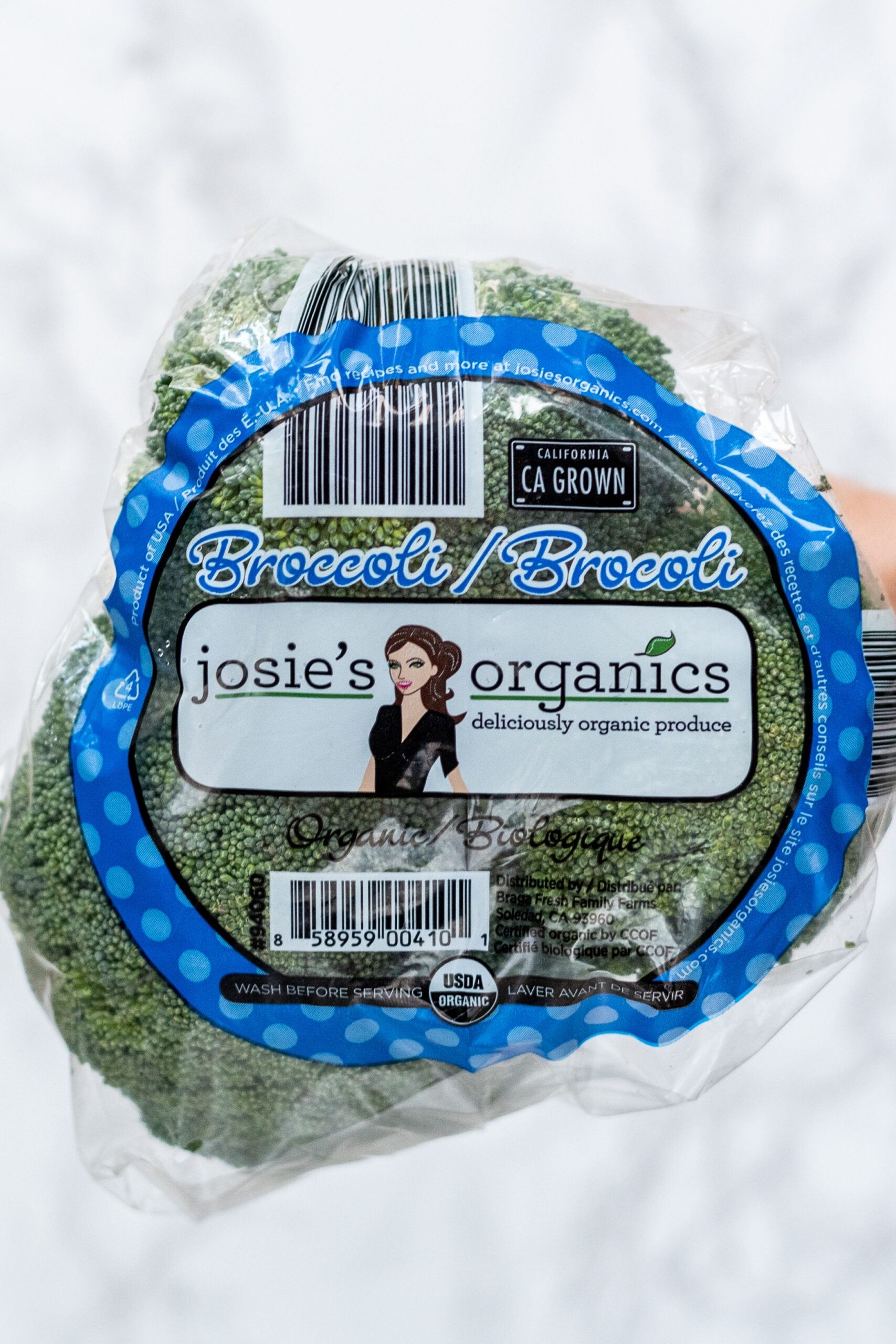 A head of broccoli with plastic wrapping on it and blue writing.