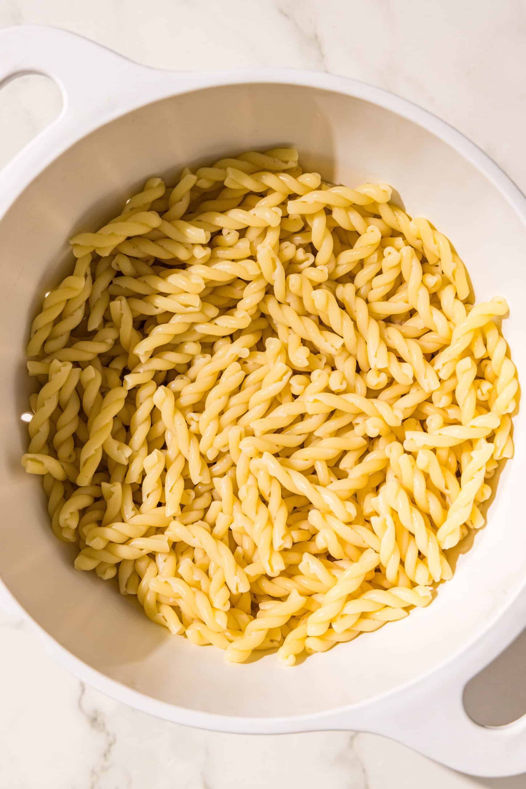 A white colander filled with cooked pasta noodles.