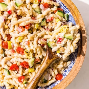 A wooden bowl filled with pasta salad and a wooden serving spoon.