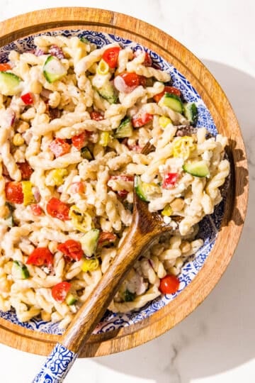 A wooden bowl filled with pasta salad and a wooden serving spoon.