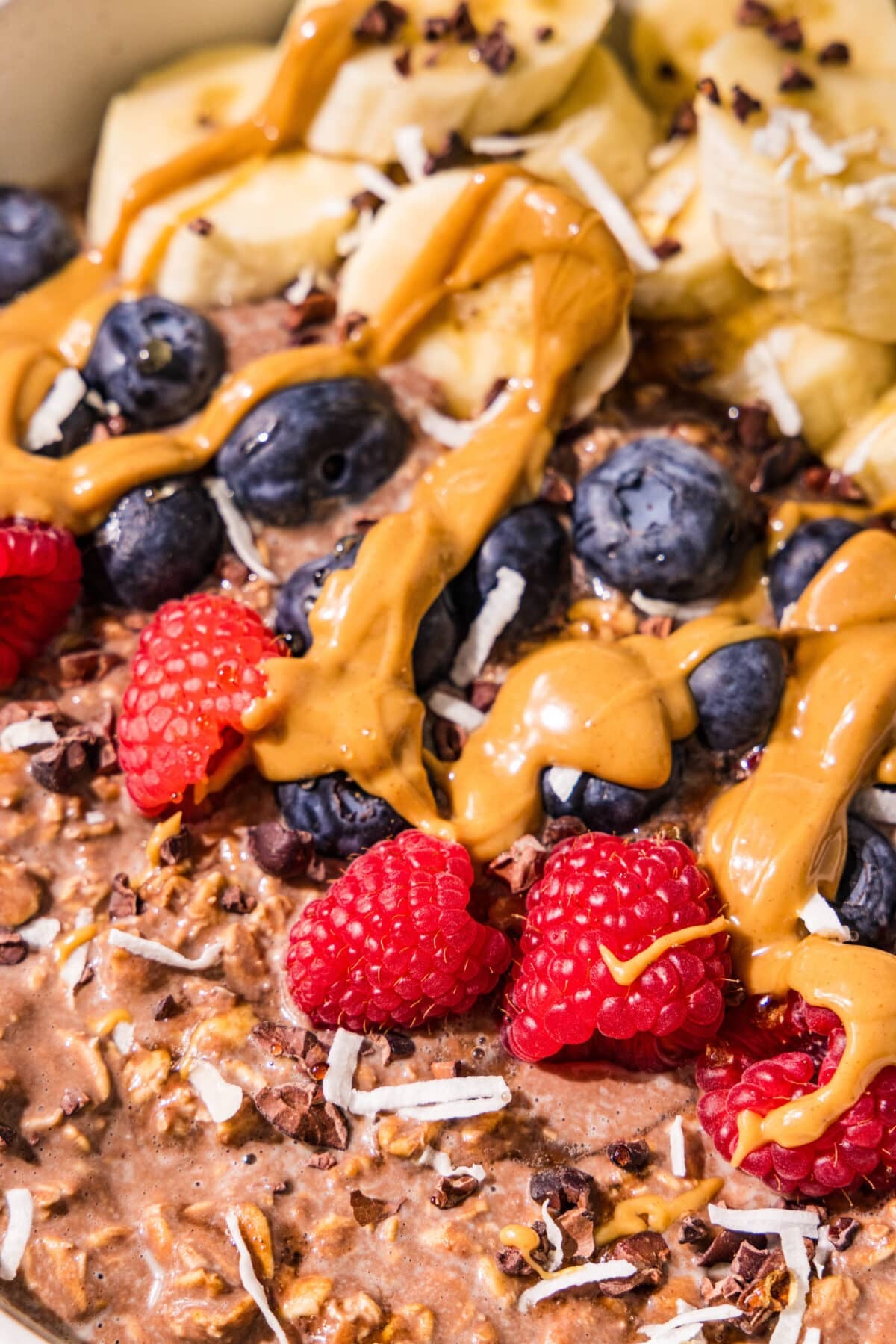 Chocolate oats topped with raspberries, blueberries, sliced banana, peanut butter drizzle, cacao nibs, and coconut.