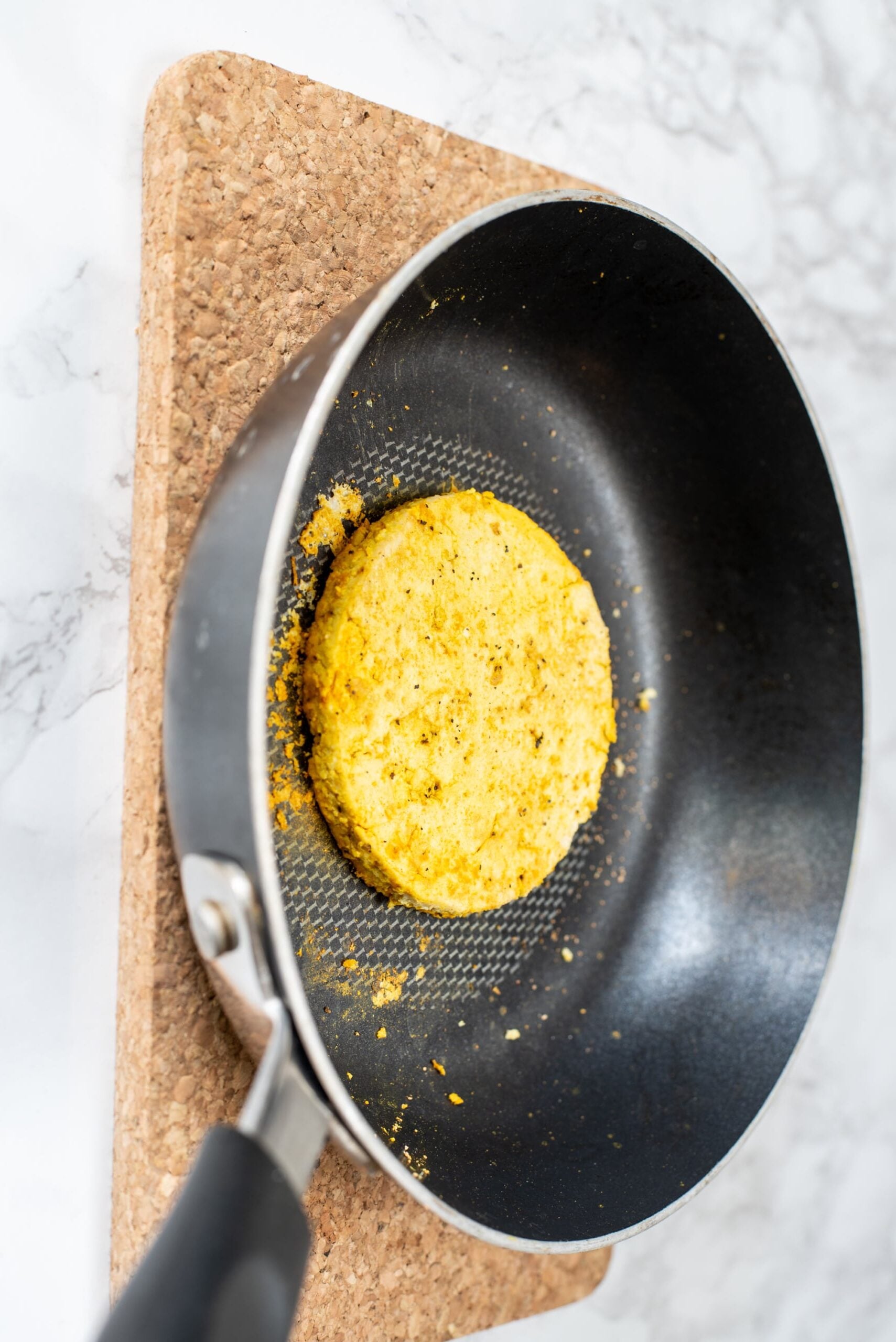 A frying pan with a piece of tofu in it.