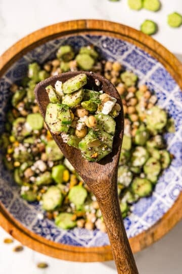 A big bowl of cucumber chickpea salad and a wooden spoon holding a scoop of the salad.