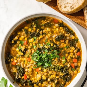 A bowl of lentil soup, a black metal spoon, and 2 pieces of bread.