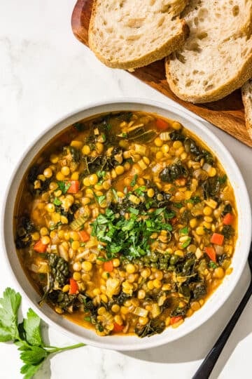 A bowl of lentil soup, a black metal spoon, and 2 pieces of bread.