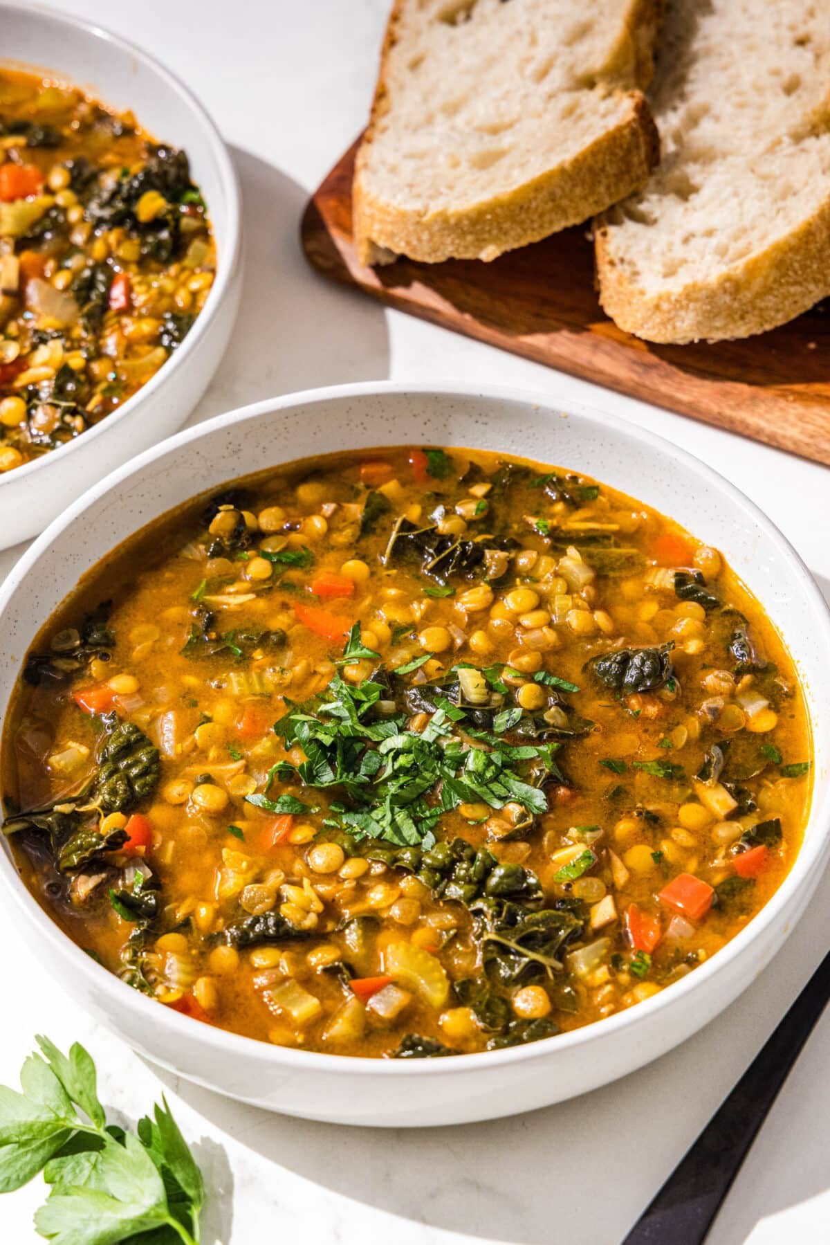 Two bowls of lentil soup topped with fresh parsley and two slices of bread.