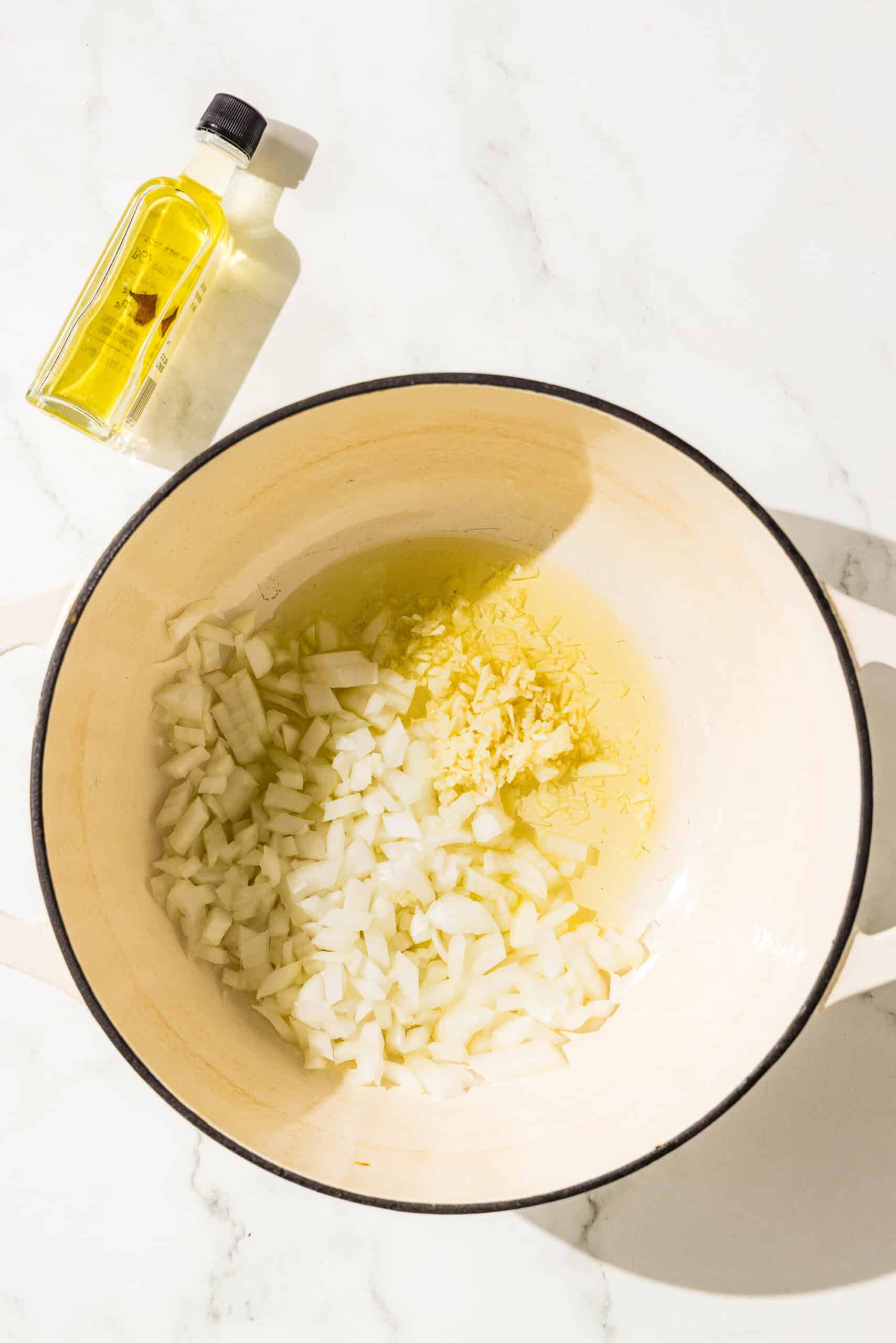 A soup pot filled with oil, garlic, and chopped onion and a small bottle of oil.